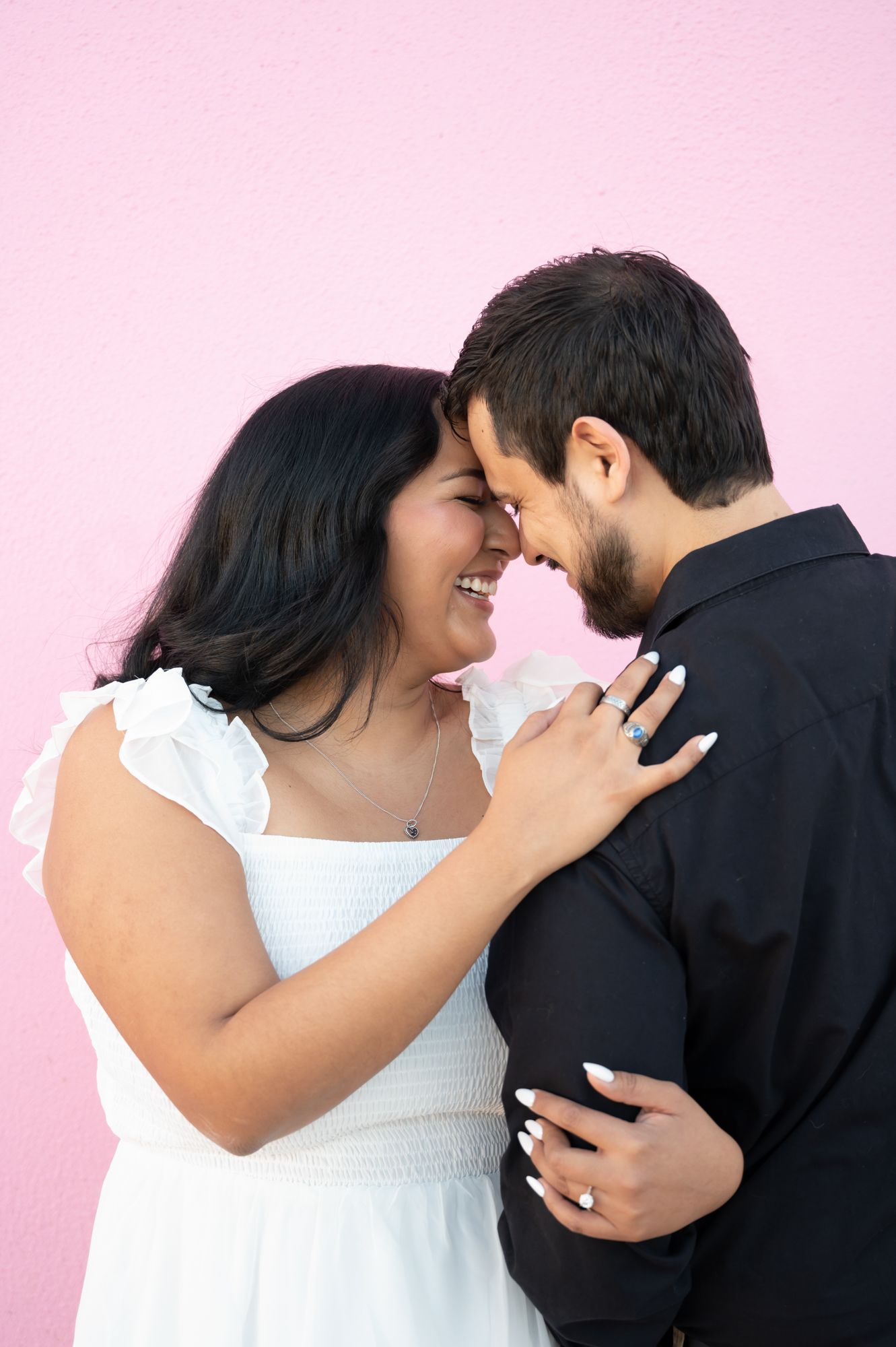 An intimate moment captured between a couple wearing black and white against a pink backdrop.