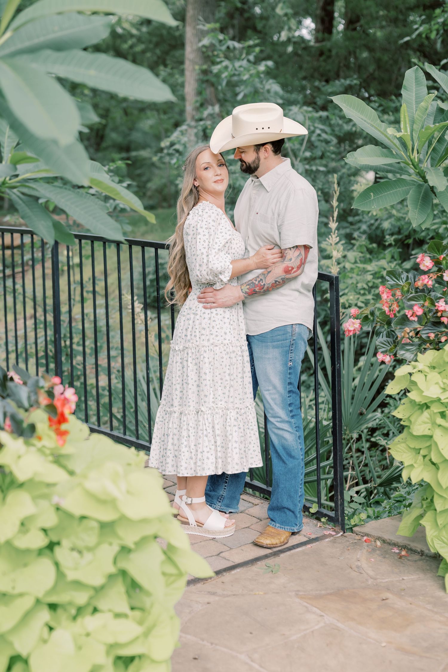Couple in country attire sharing a tender moment by a garden gate.