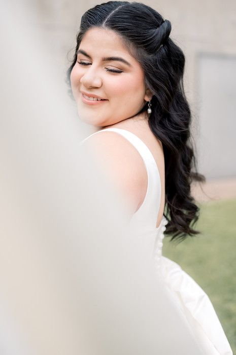 Close-up portrait of smiling bride with dark wavy hair and drop earrings in white wedding gown.