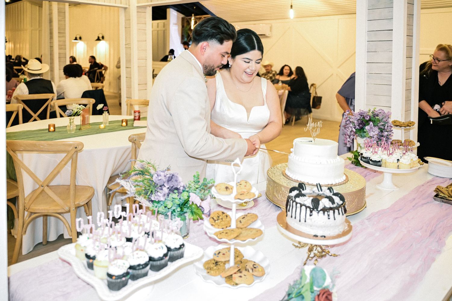 Wedding reception dessert table featuring multiple cakes and treats with floral decorations.