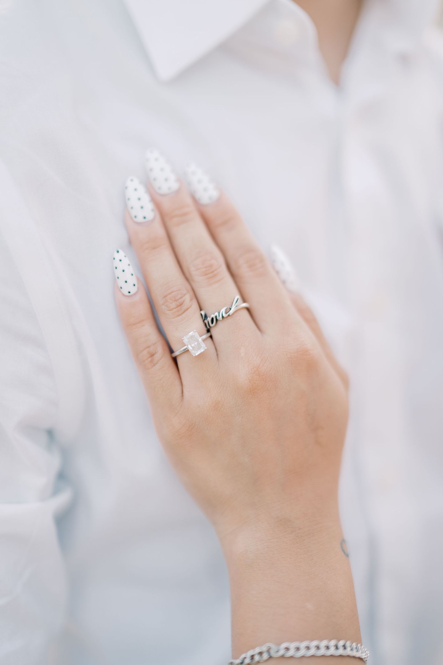Close-up of an engagement ring and name ring on a bride-to-be's hand with white nails.