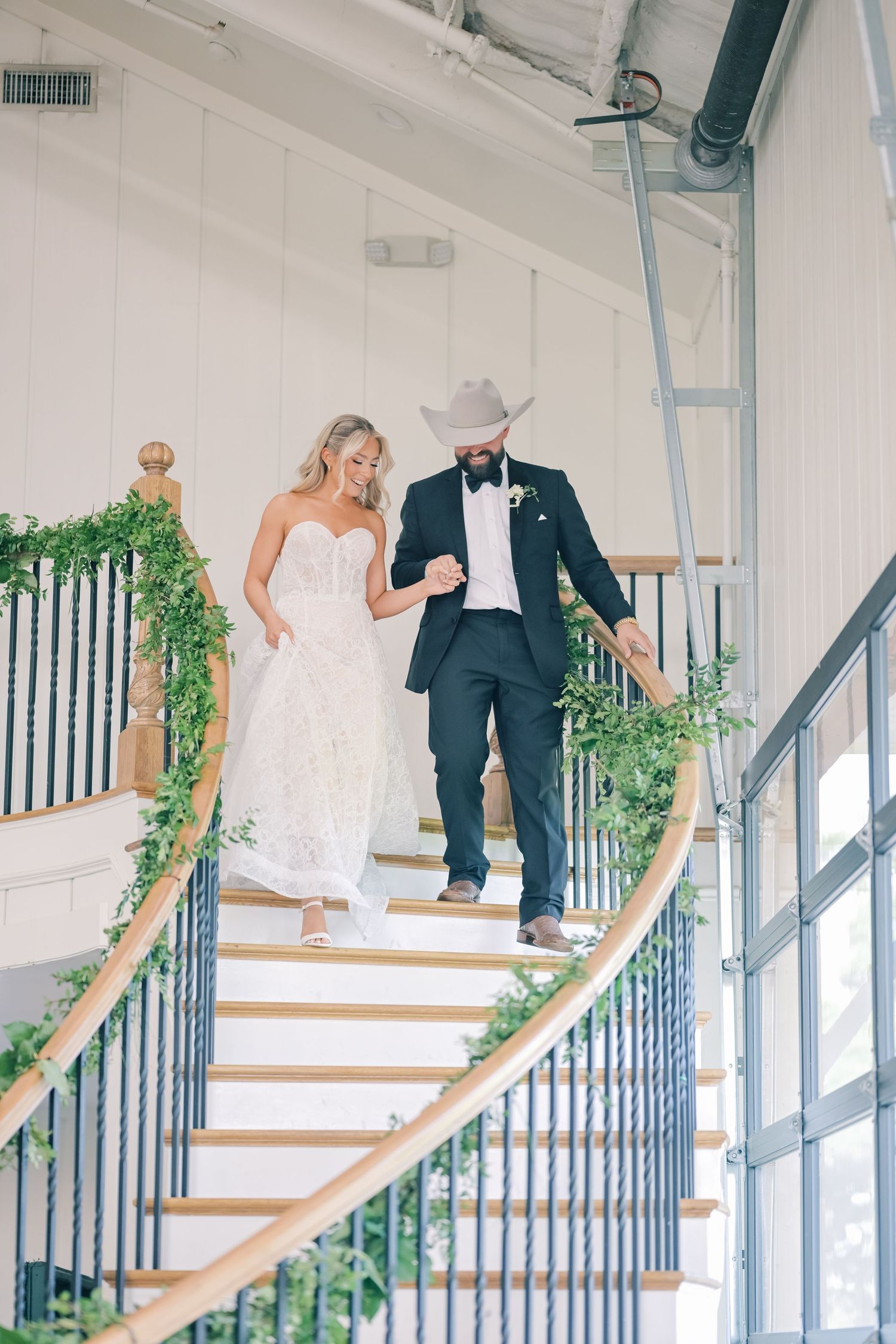 Bride and groom descend elegant spiral staircase decorated with greenery garland.