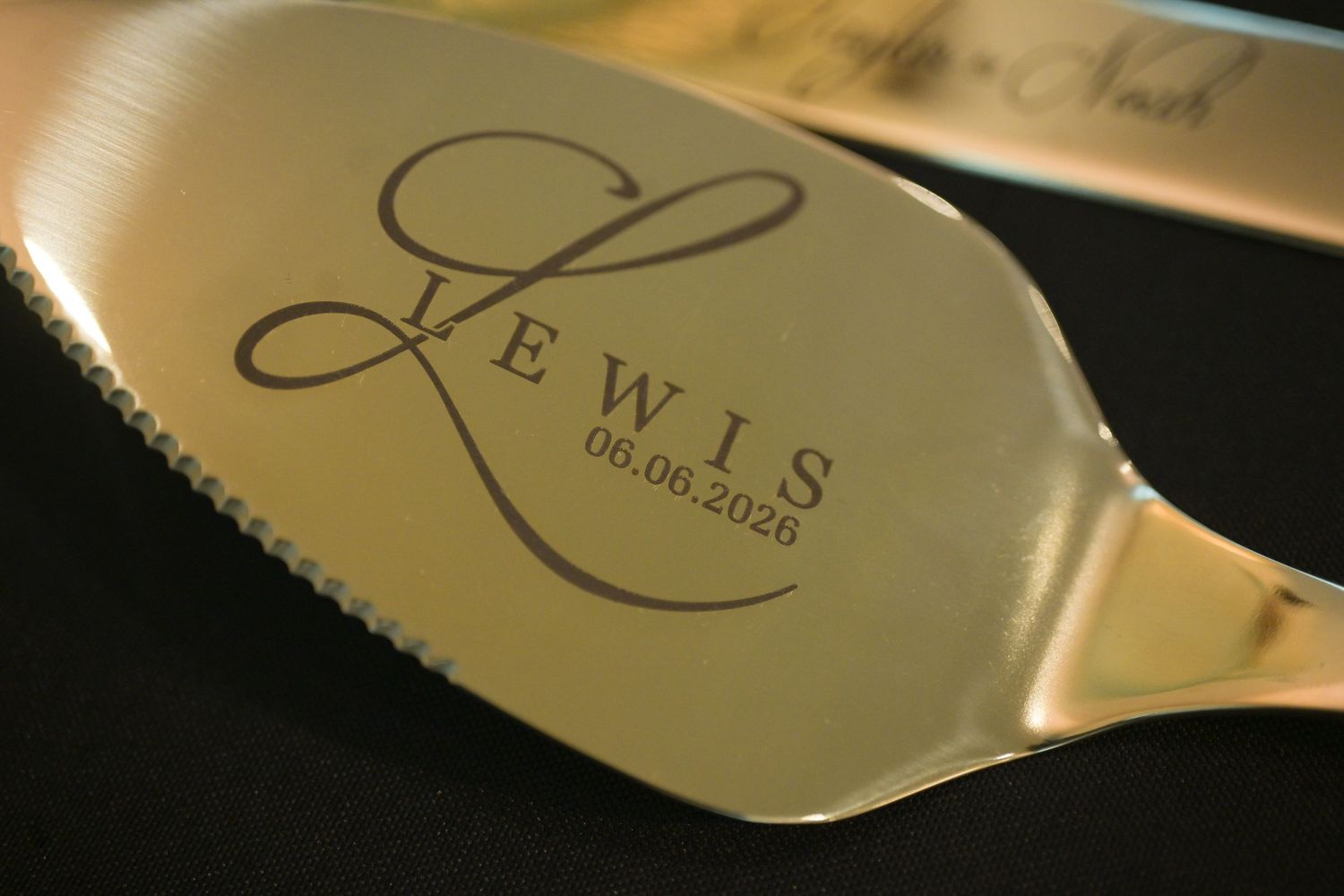 Gold engraved cake server with Lewis monogram and wedding date 06.06.2026 detail shot.