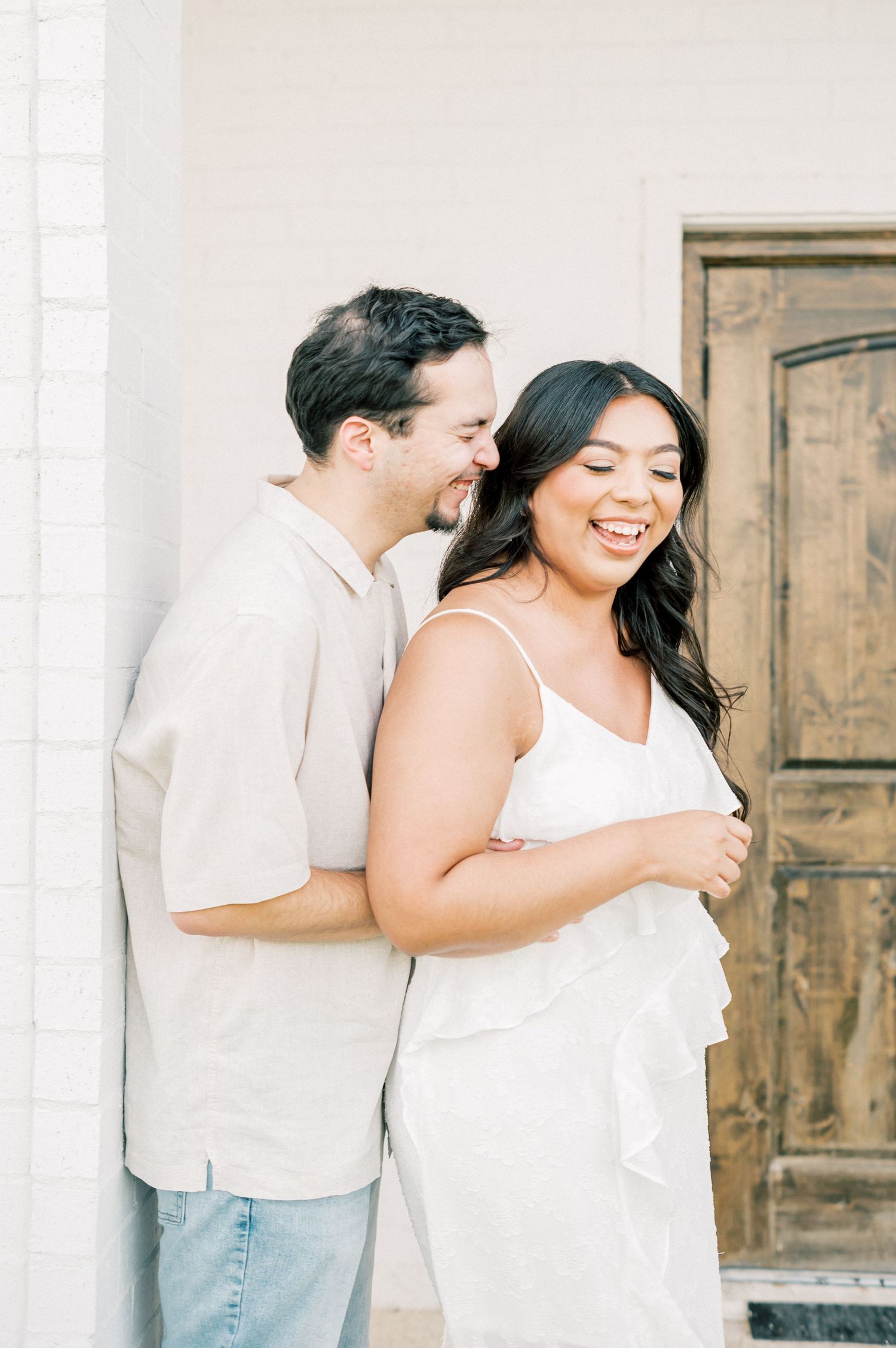 A couple embraces and laughs together during a casual maternity photography session outdoors.