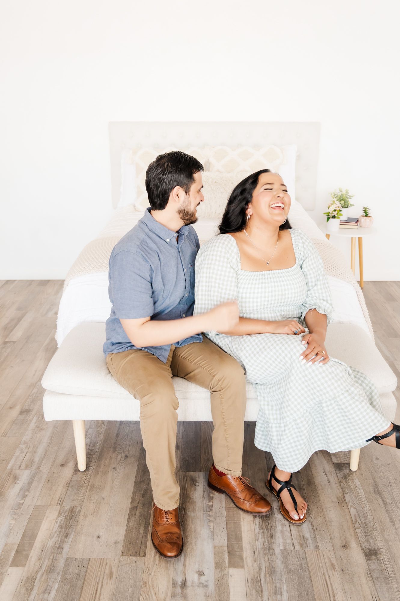 Couple sharing a lighthearted moment while sitting together on white bench with wooden floors.