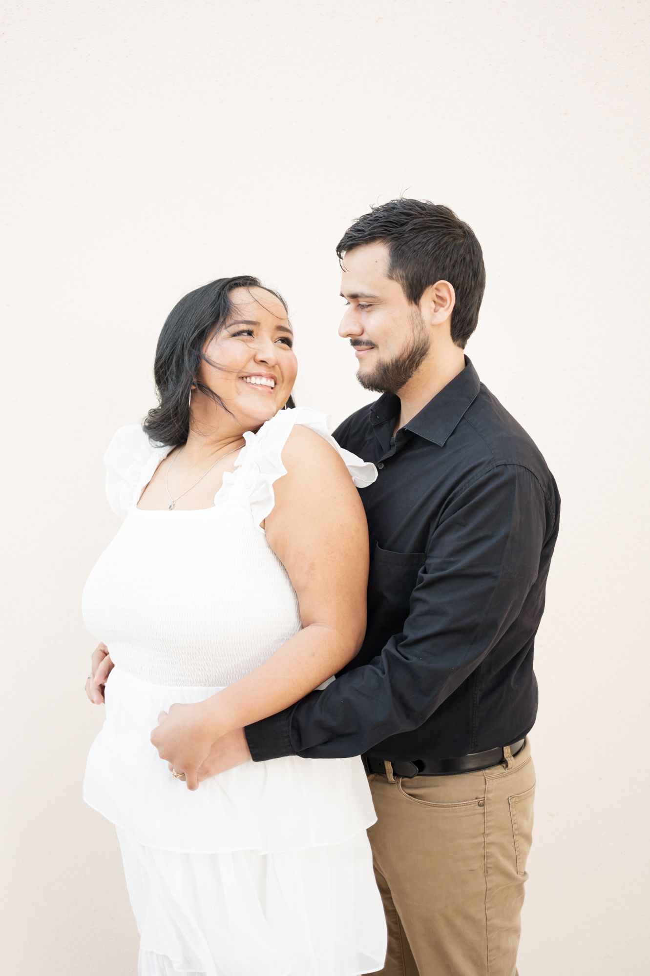 A joyful couple shares laughter while embracing in a bright white studio space.