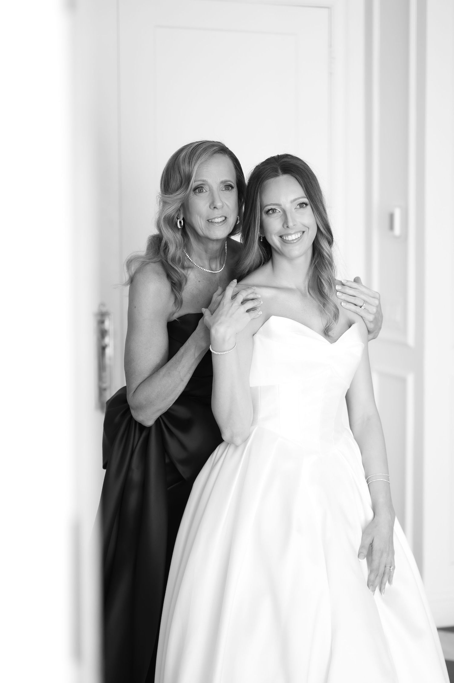 Black and white photo of bride in strapless gown with older woman in dark dress placing hands on her shoulders.