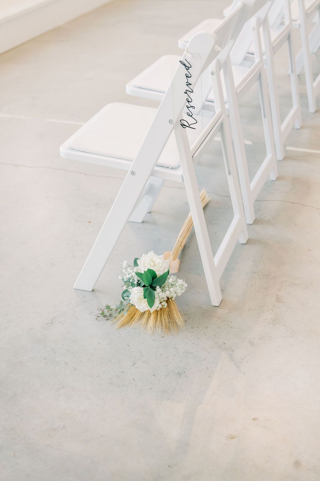 White folding chairs with Reserved sign and small bouquet of white flowers on concrete floor.