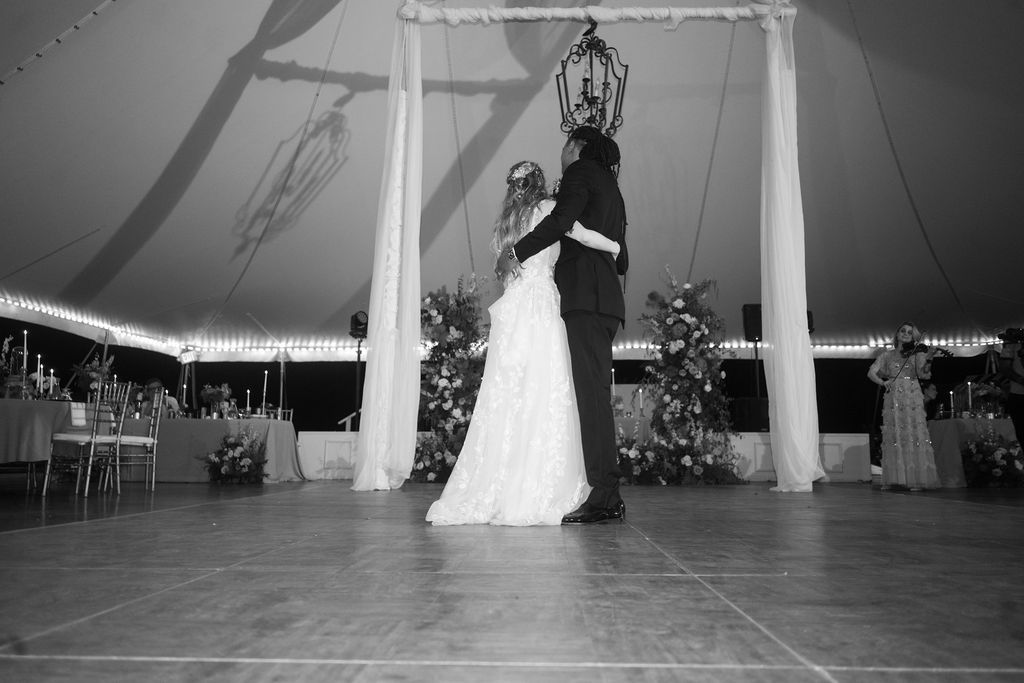 Bride and groom share first dance under elegant tent with string lights at wedding reception.
