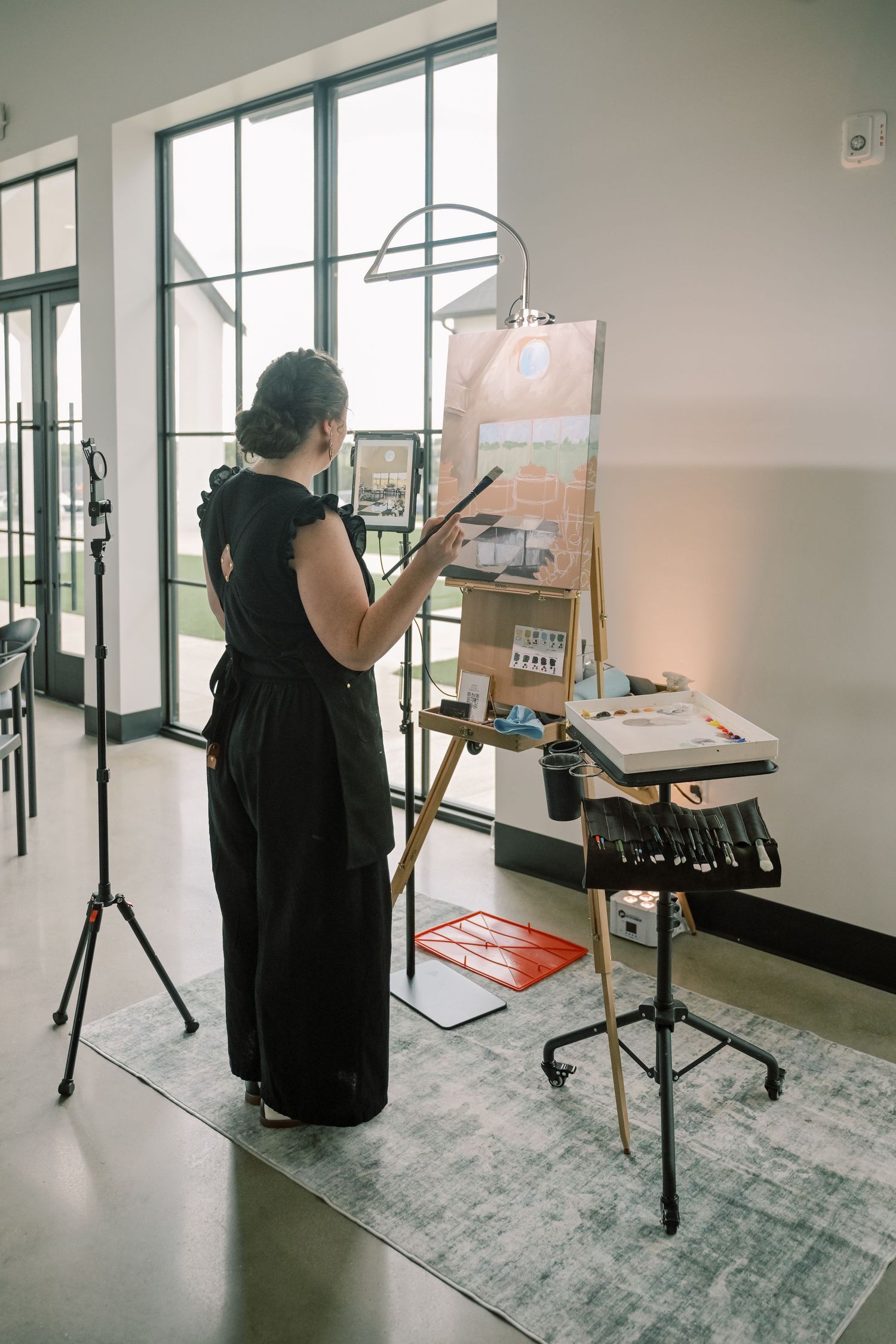 Live wedding painter in black outfit working on a canvas at an easel during a reception.