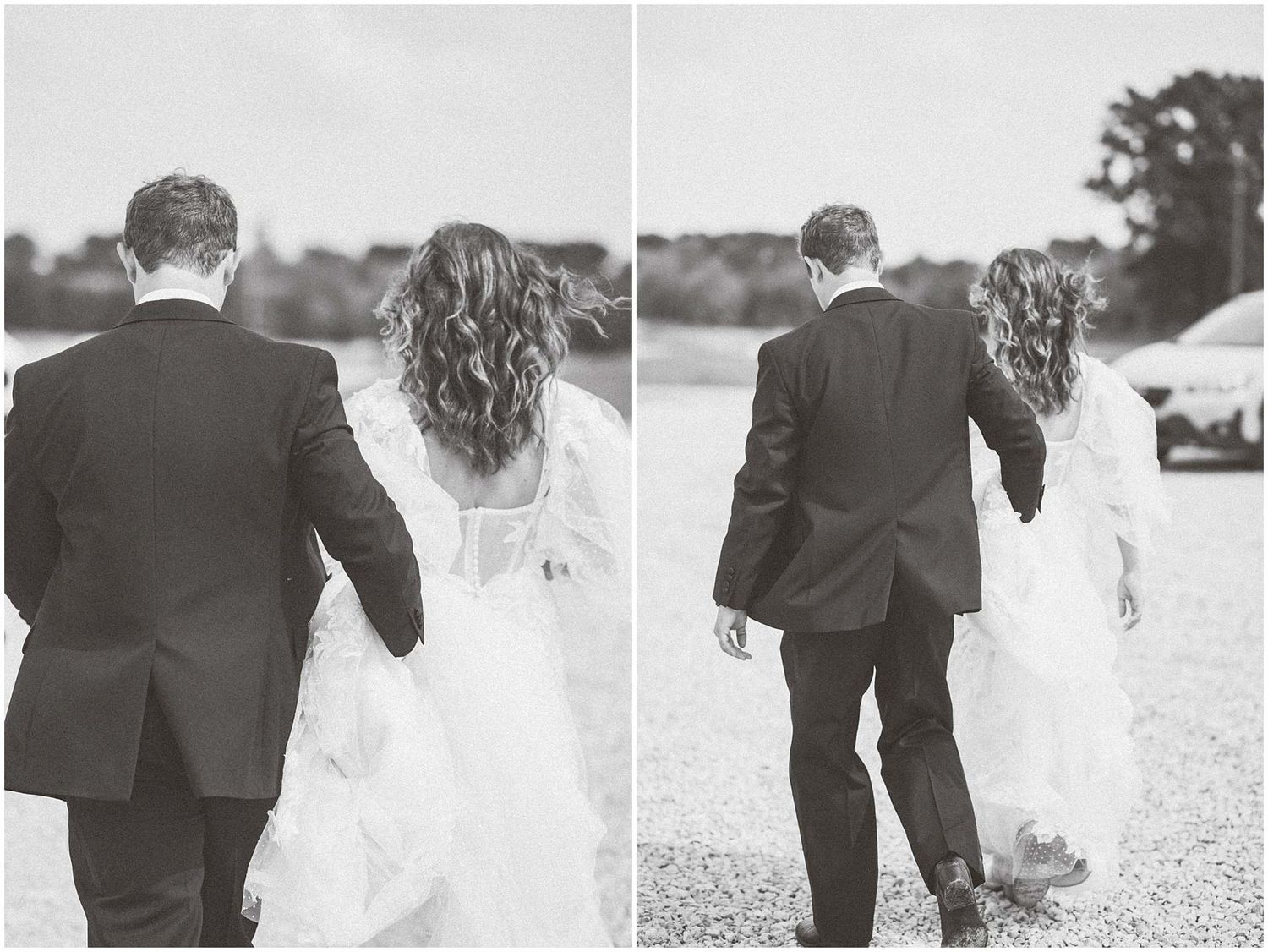 Bride and groom walk hand in hand along a lakeside path in black and white.