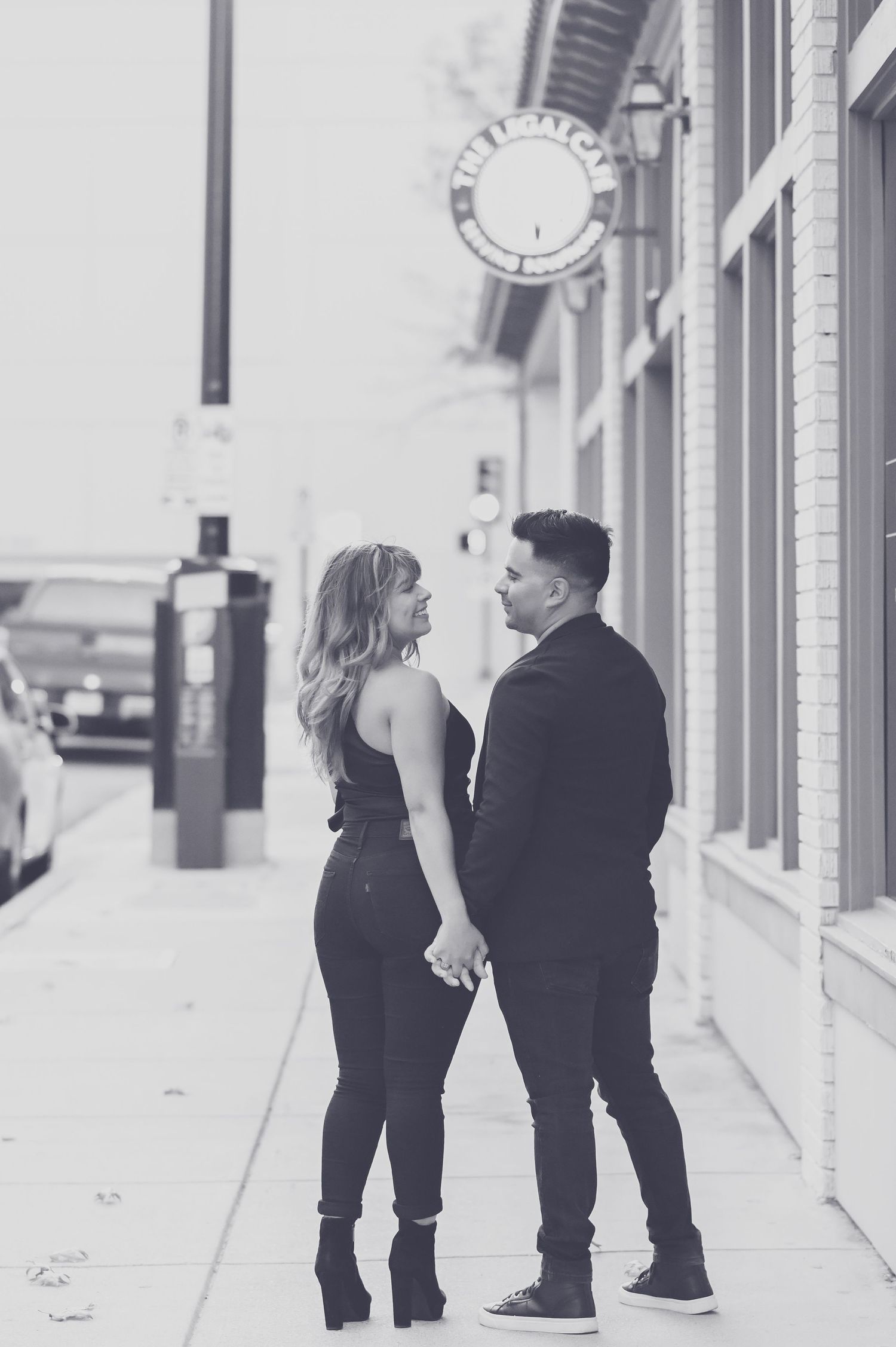 Black and white photo of a couple holding hands and gazing at each other on a city sidewalk.