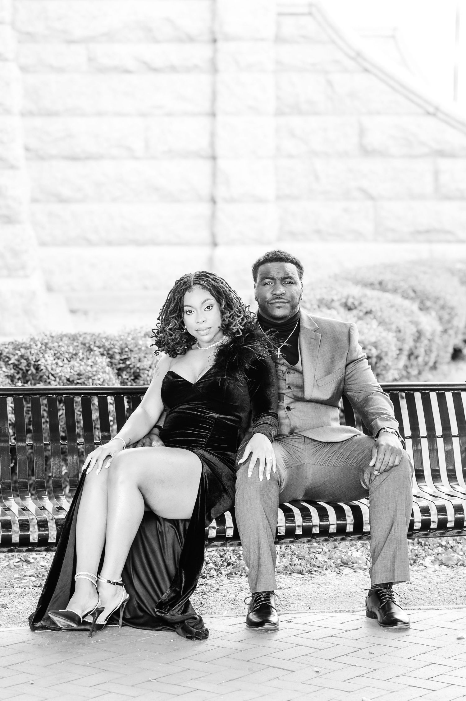 Elegant couple in formal attire posing on a bench in black and white portrait photography.