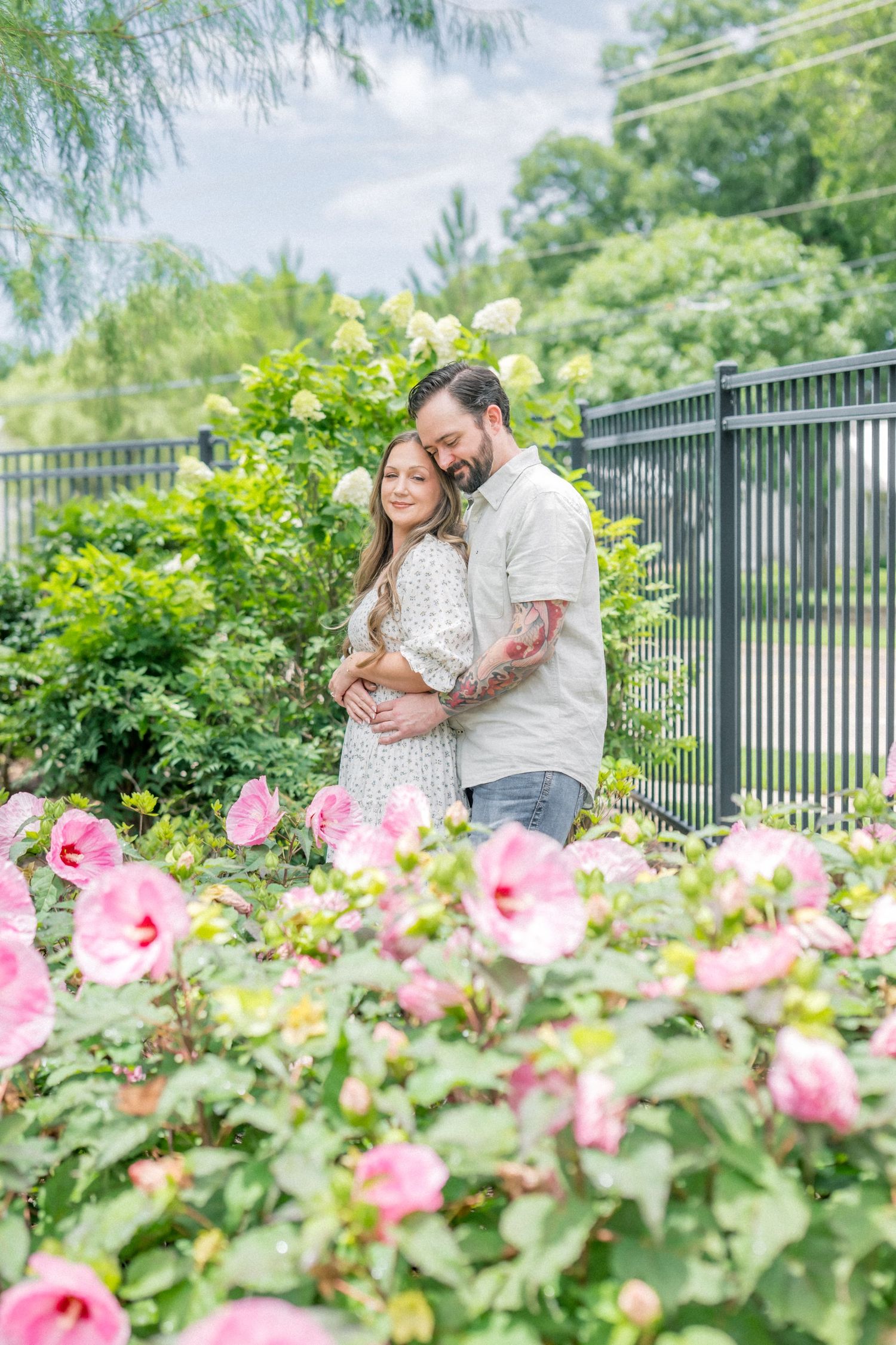 Romantic couple embracing in a garden with pink roses blooming in the foreground.
