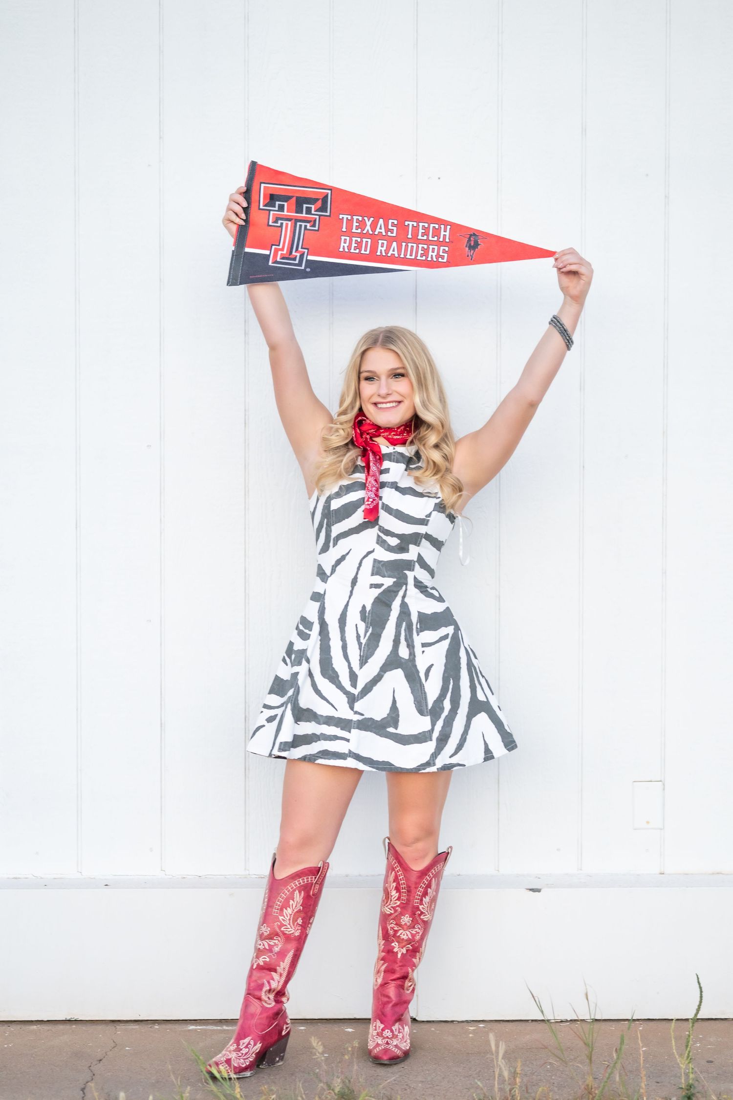 Blonde woman in zebra dress holding Texas Tech Red Raiders pennant wearing red cowboy boots.