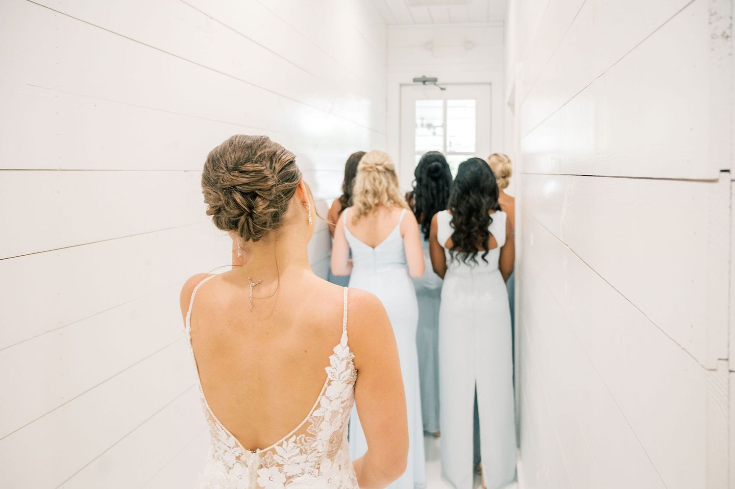 People helping with final adjustments to a white wedding dress in a bright room.