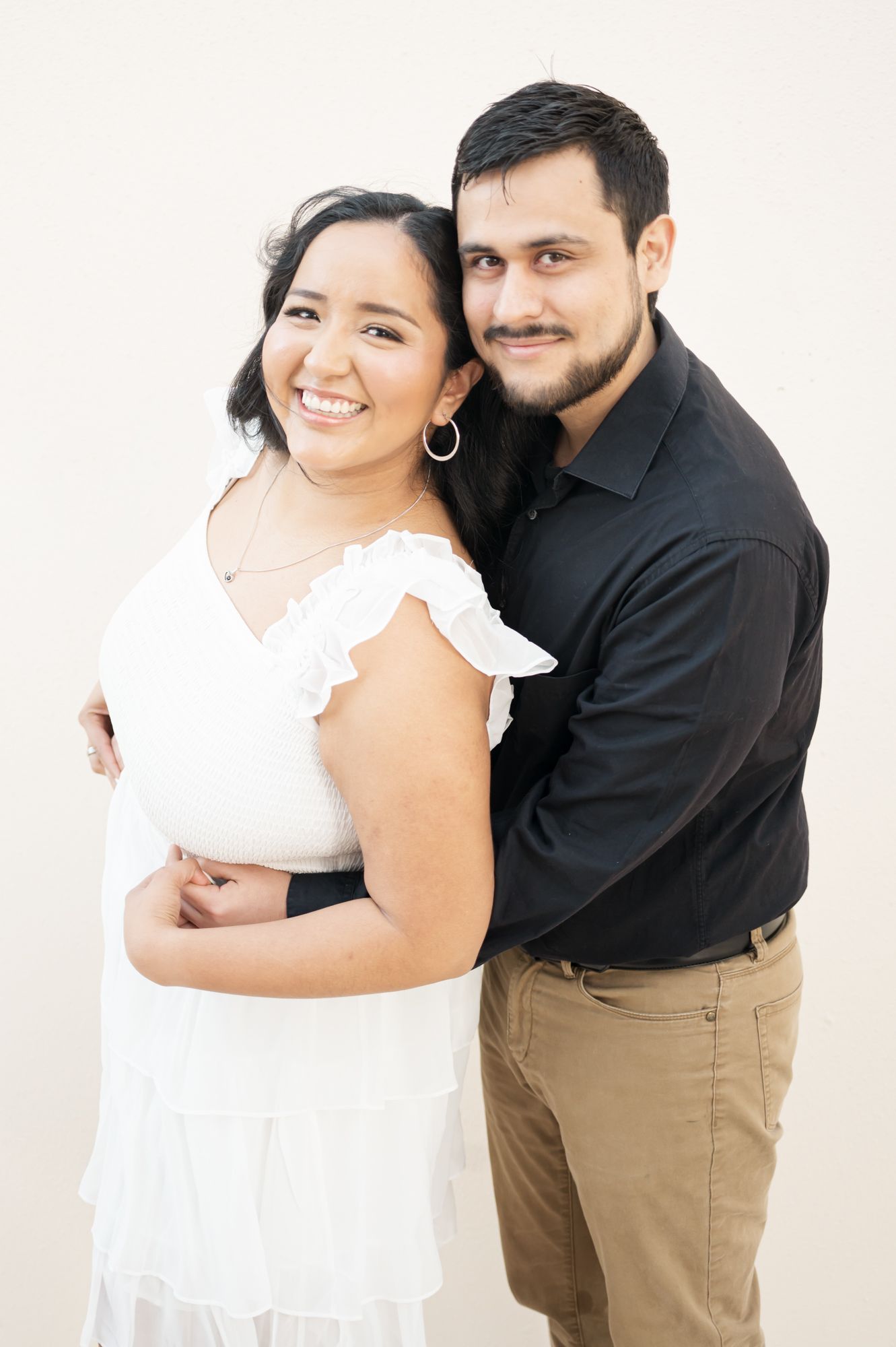 A couple in white and black outfits posing against a white backdrop in a romantic photoshoot.