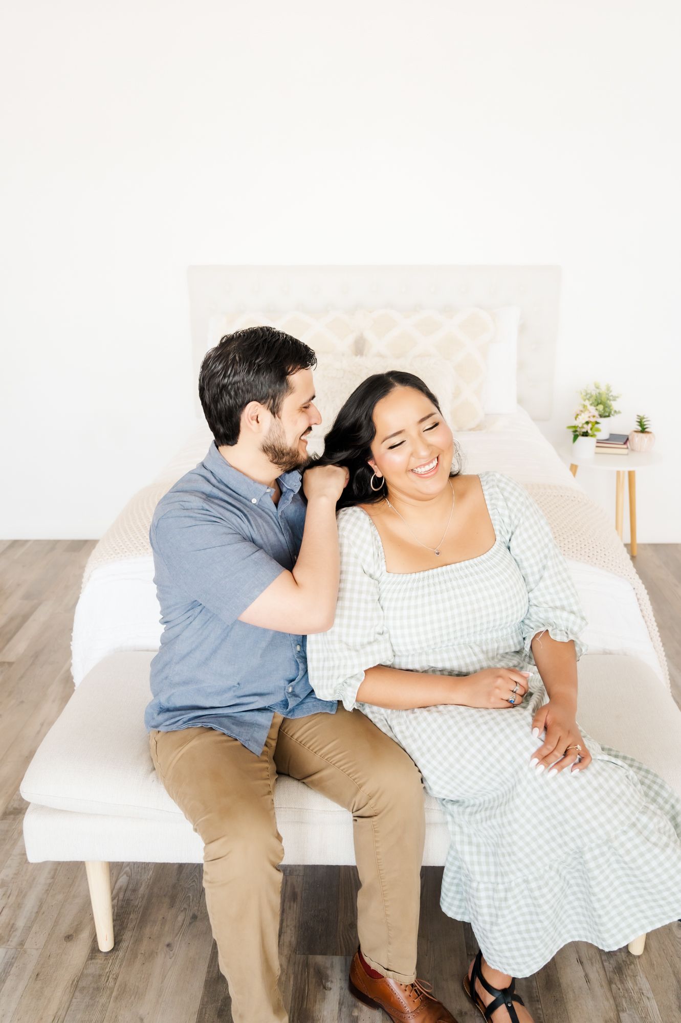 Happy couple sharing intimate moment while sitting on white bench in bright studio.