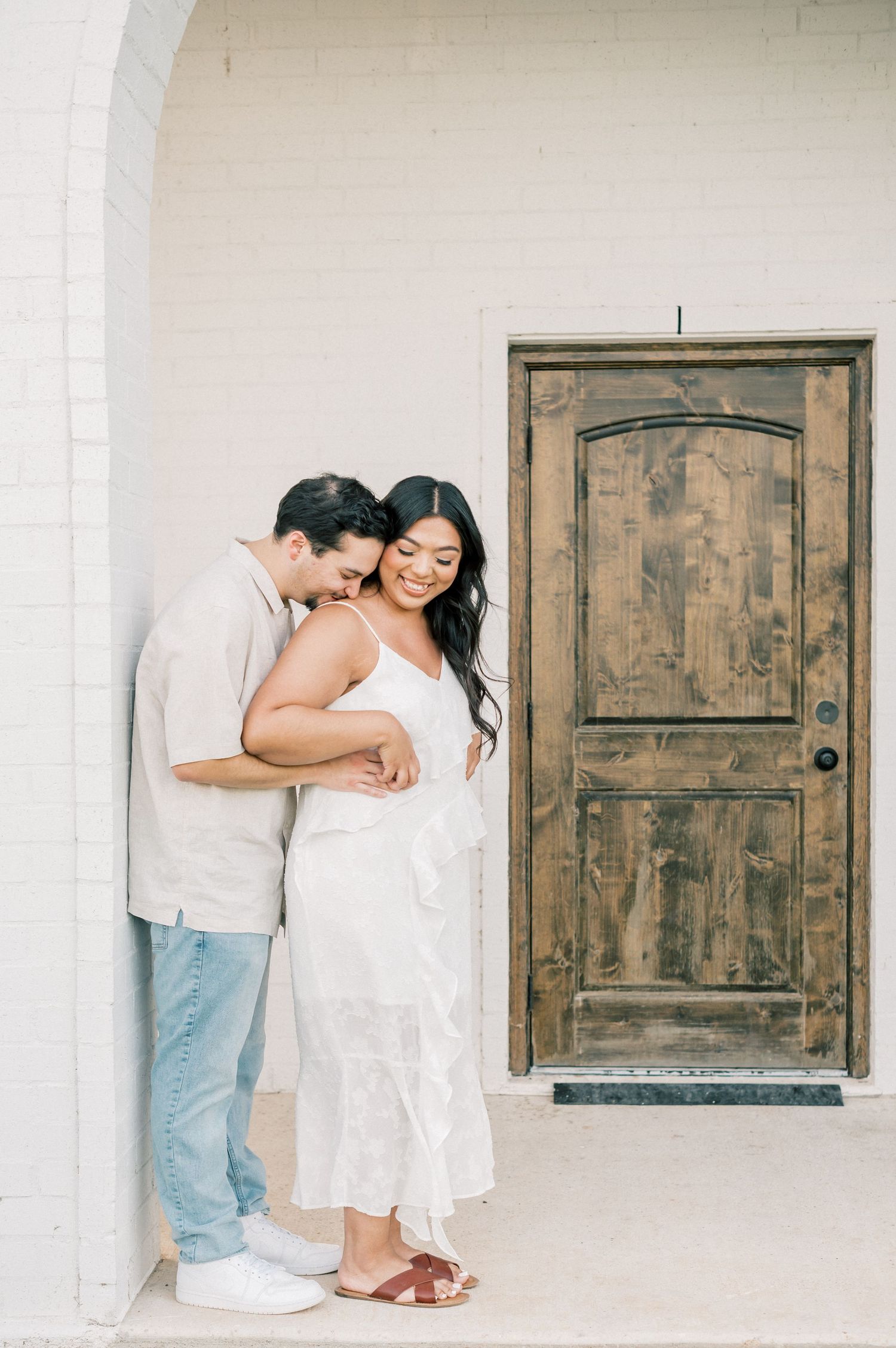 A couple shares tender romantic moments against a white wall with rustic wooden doors in a minimalist setting.