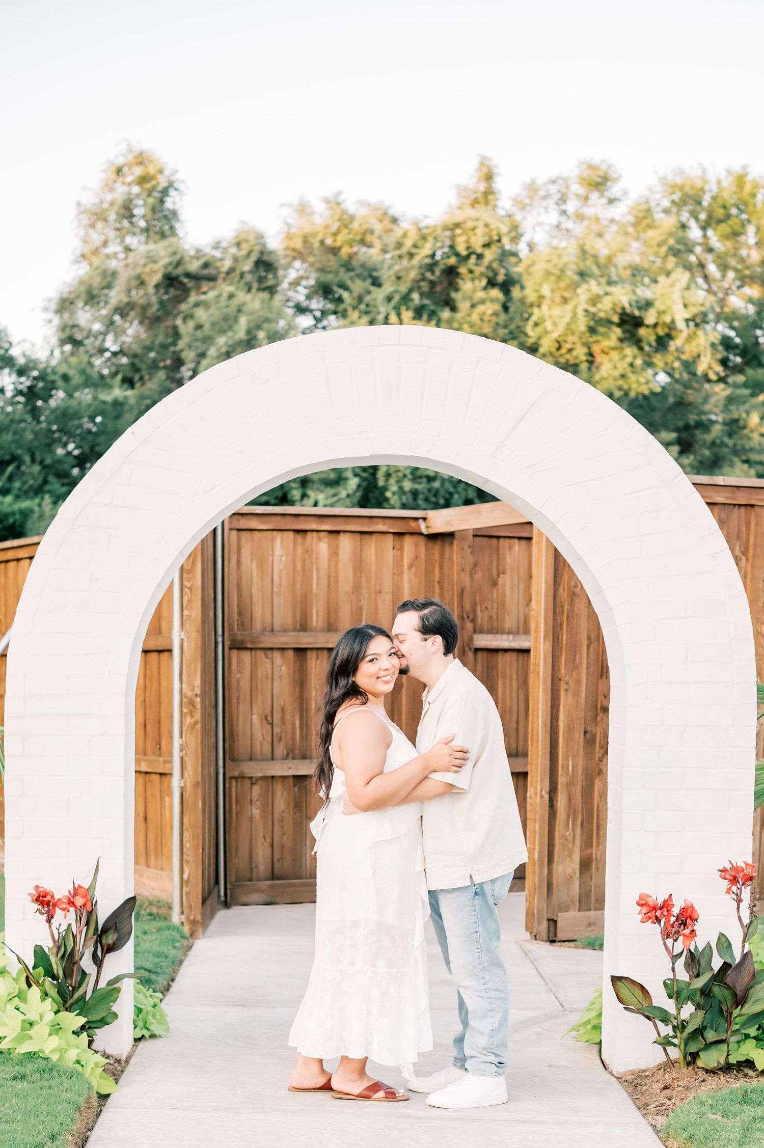 A couple shares romantic moments in a backyard garden setting with wooden fencing and archways.