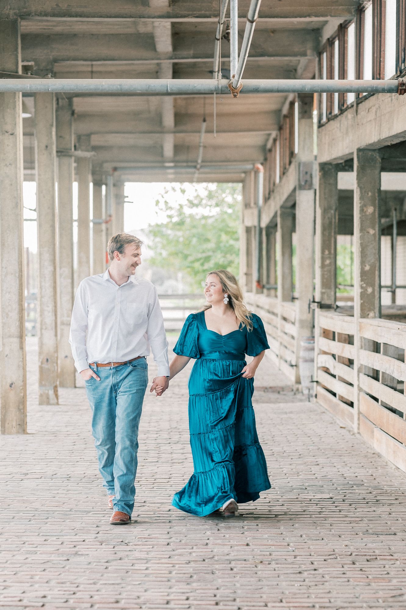 A couple walks hand in hand through a covered brick walkway, with the person in a teal maxi dress and other in casual attire.