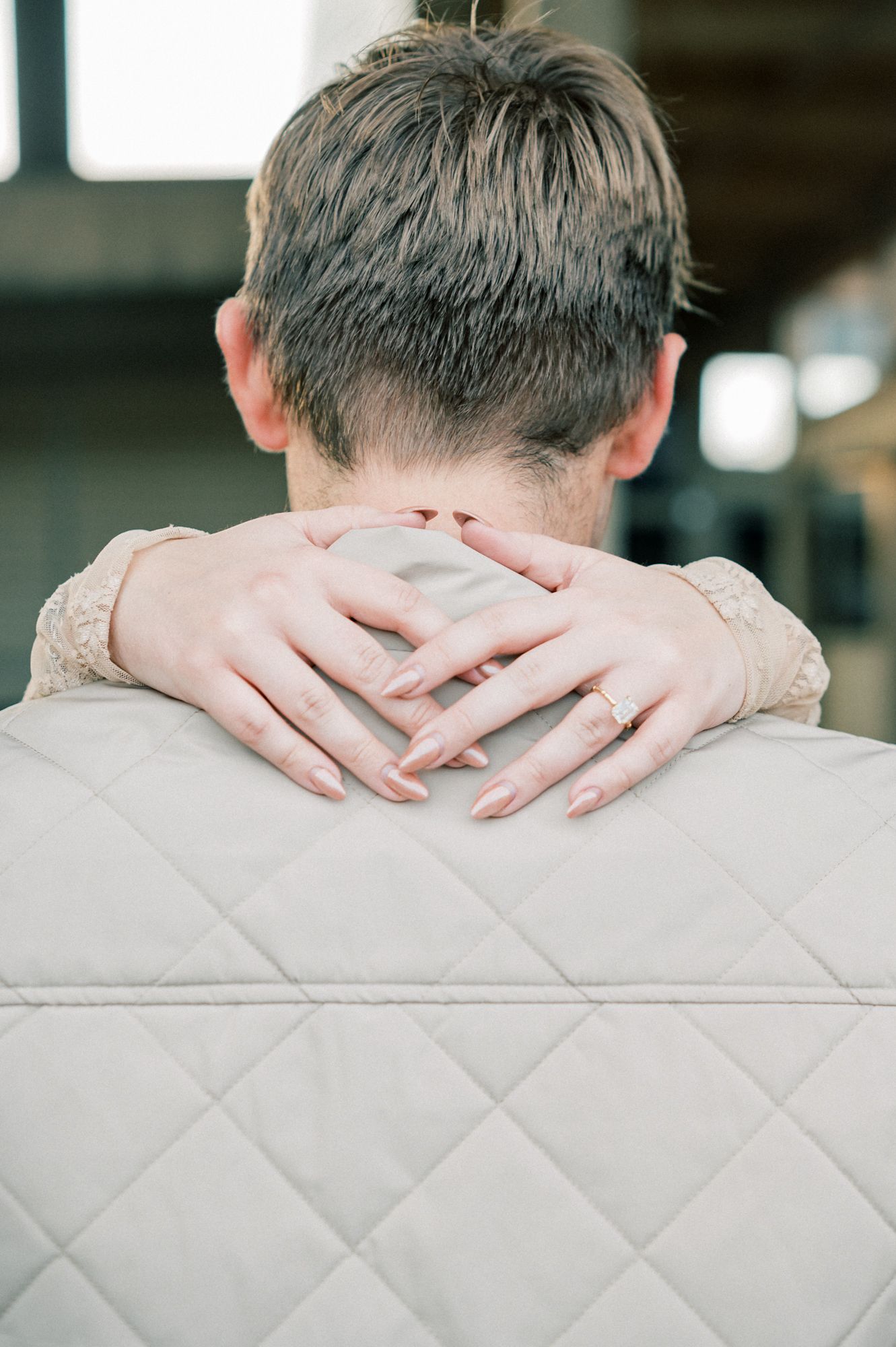 Hands lovingly embracing around shoulders against a quilted background.