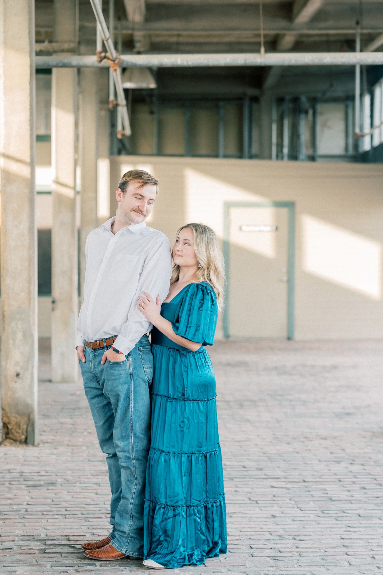 A couple shares joyful moments together in an industrial setting with concrete floors and pillars.