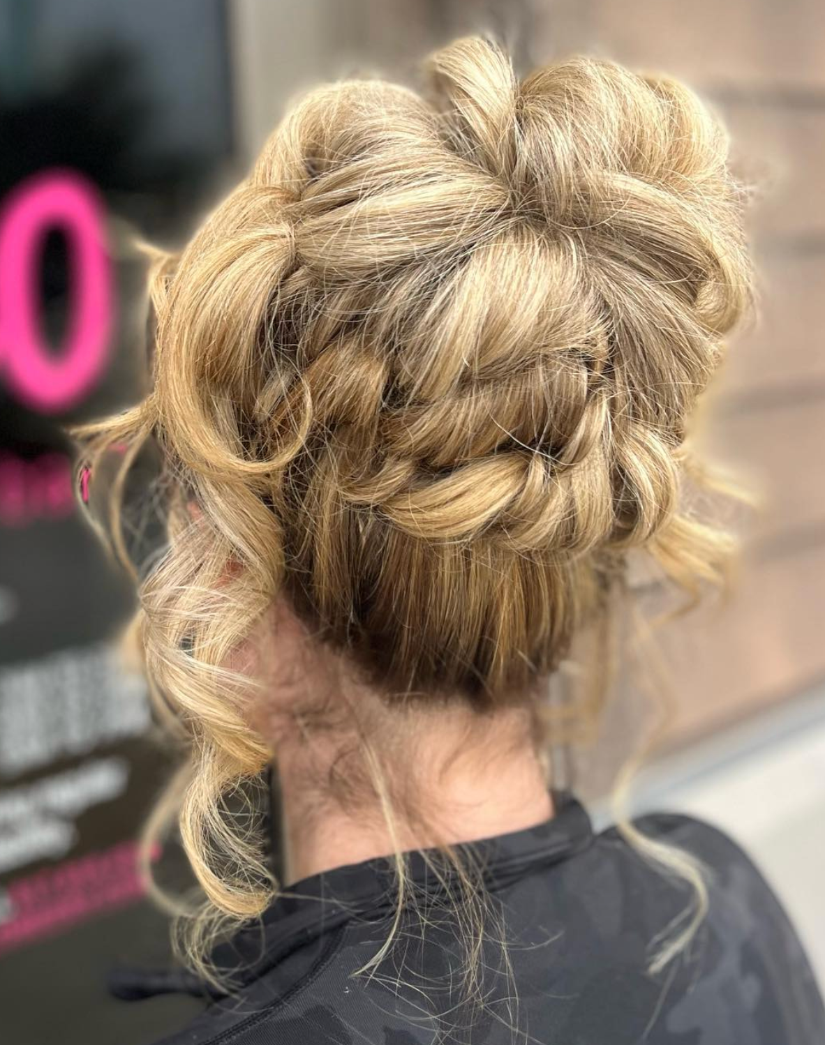 Elegant blonde updo hairstyle with braided details and loose curls, styled at a salon.