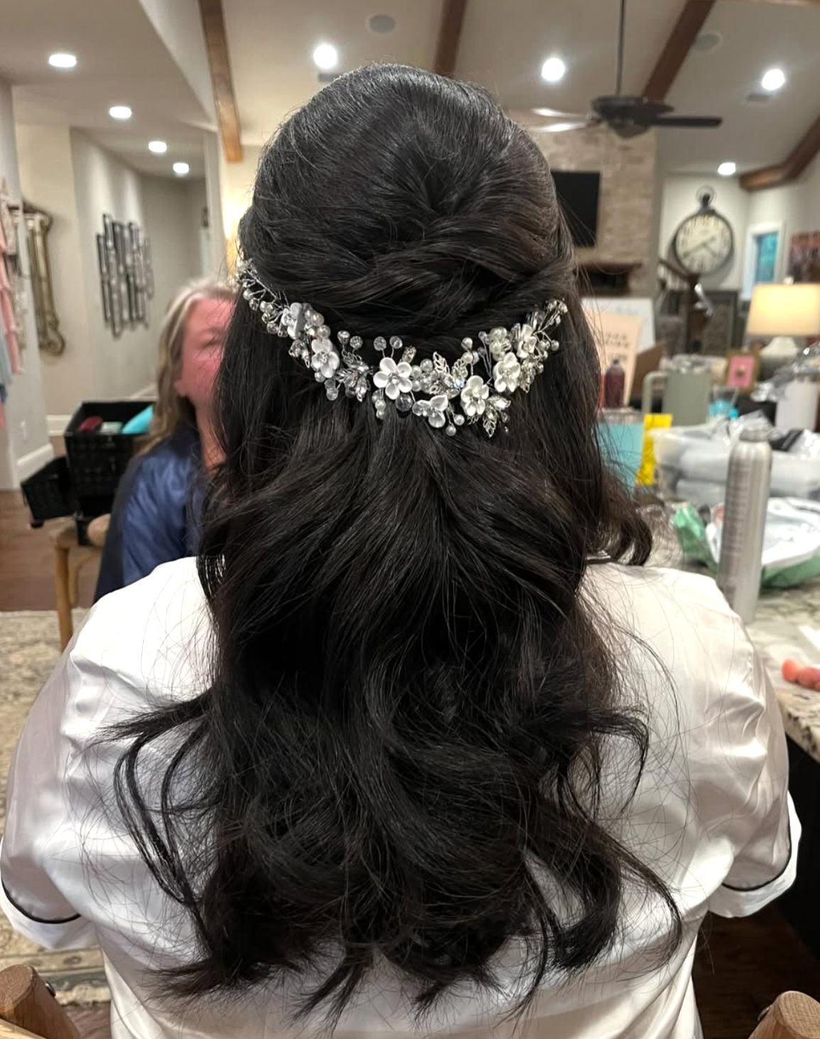 Bridal half-up hairstyle with dark wavy hair adorned with a crystal floral hair vine accessory.