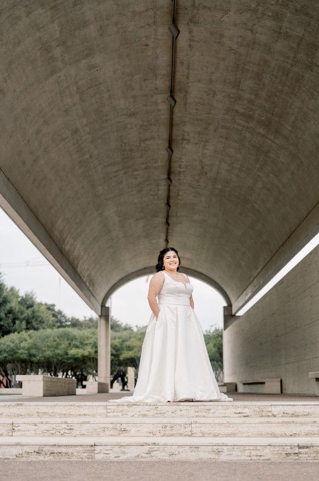 Bride in white gown standing under curved concrete arch on steps.