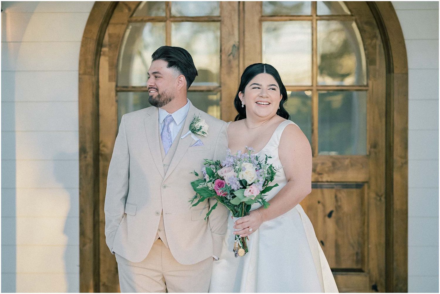 Wedding couple poses for portraits in front of grand wooden arched doorways.