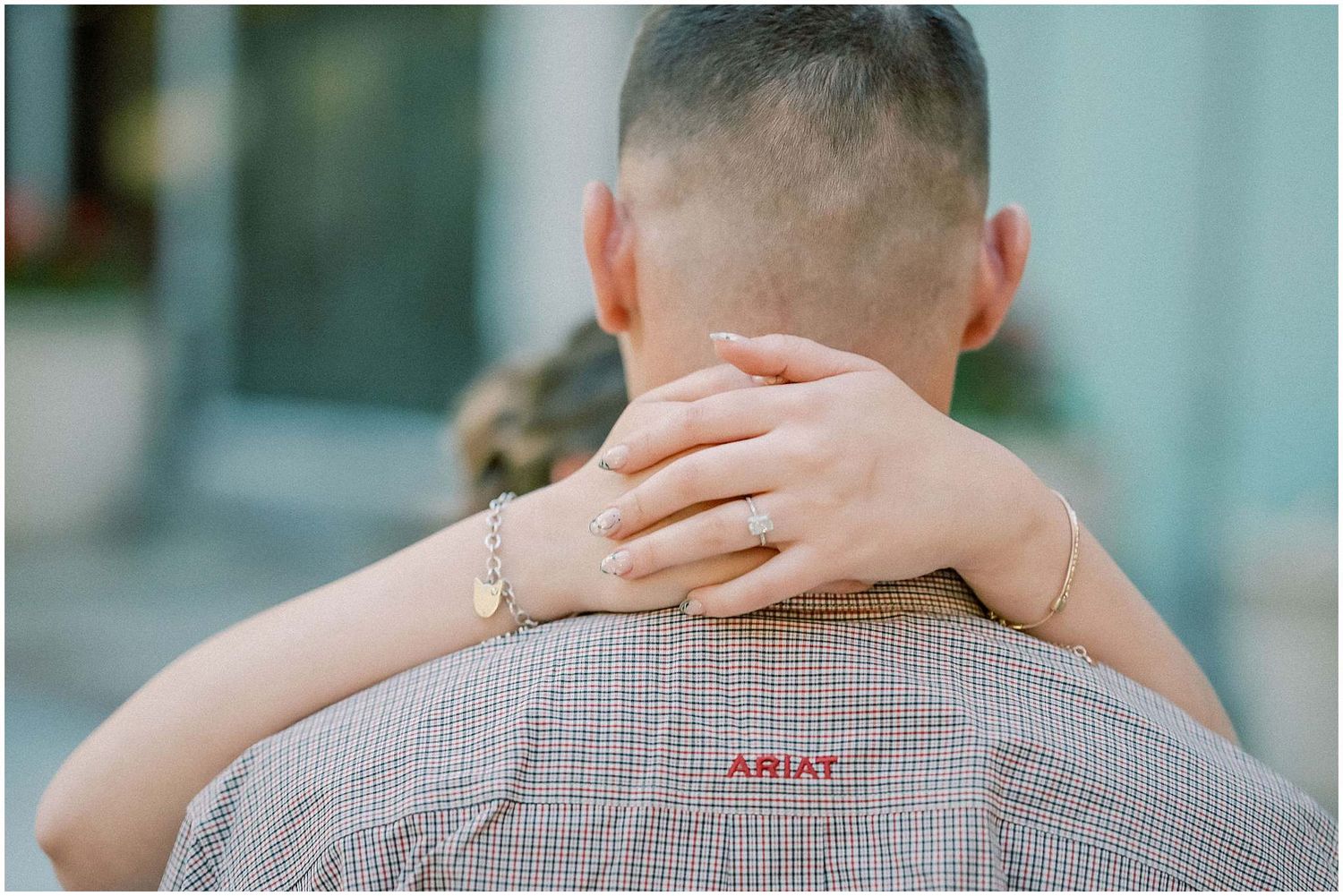 A close-up shot showing hands embracing with a wedding ring visible against a checkered shirt.