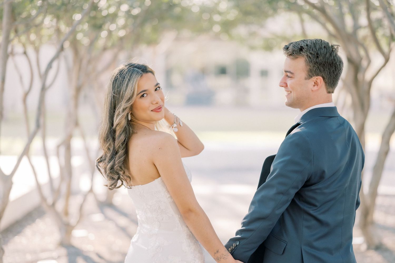 A romantic couple in wedding attire embrace and dance together in a sunlit outdoor setting.