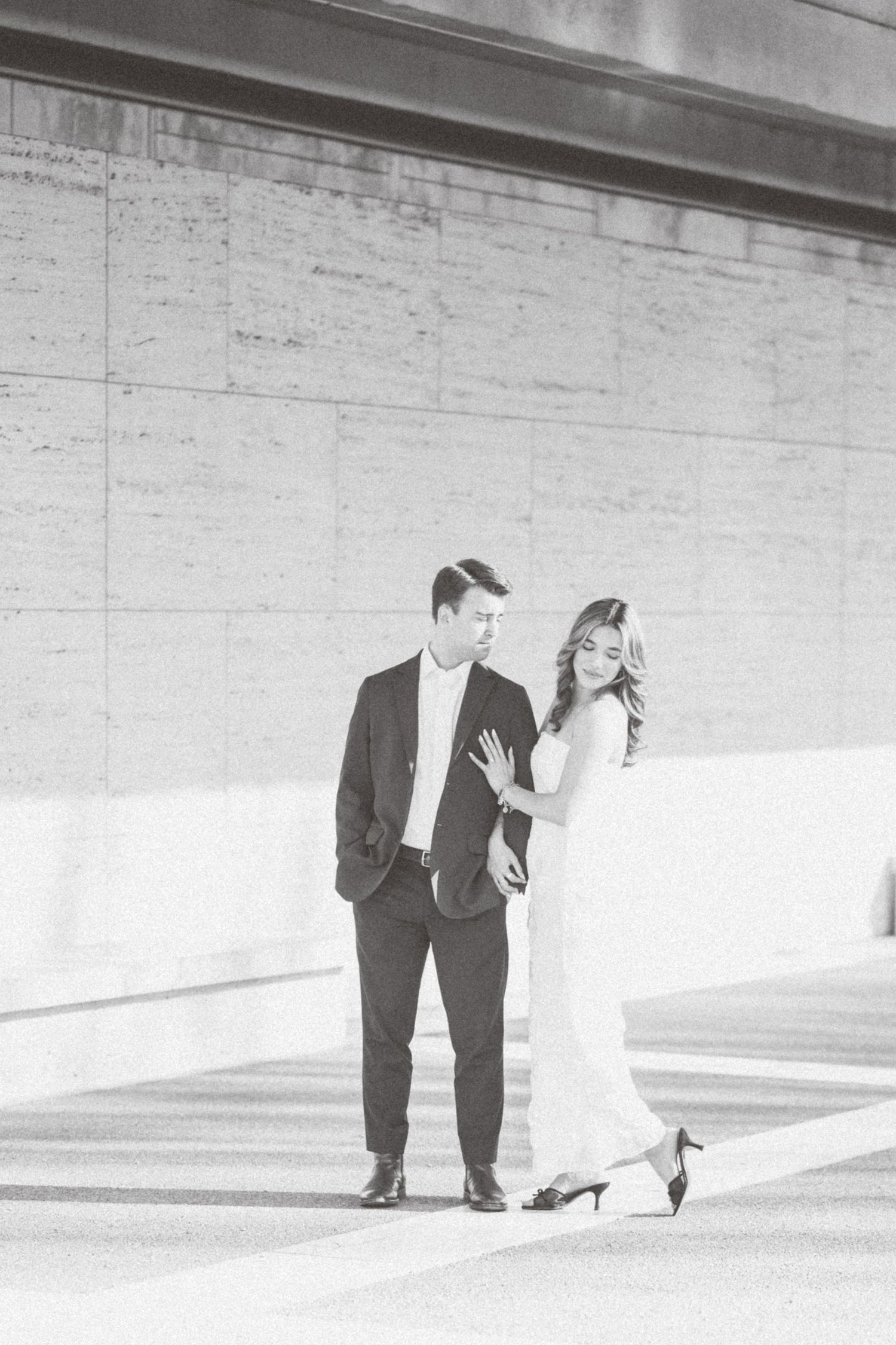 A couple in formal attire shares a playful moment in a minimalist white architectural space.