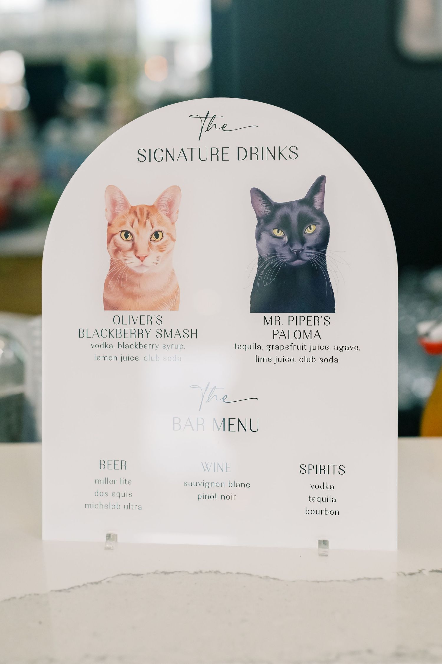 Wedding signature drinks menu featuring illustrated cats Oliver and Mr. Piper on an arch-shaped acrylic sign.