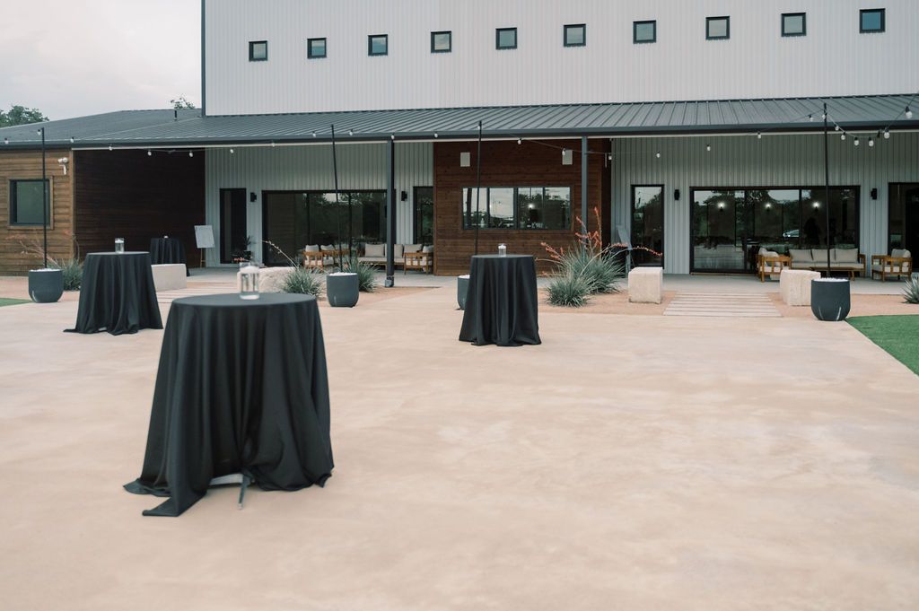 Outdoor patio venue with black cocktail tables, string lights, and modern building backdrop for elegant events.