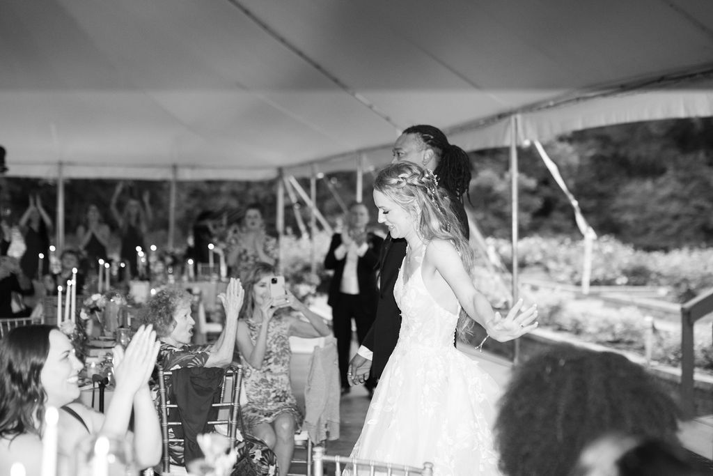 Black and white photo of a bride and groom making a grand entrance at their elegant tented wedding reception.