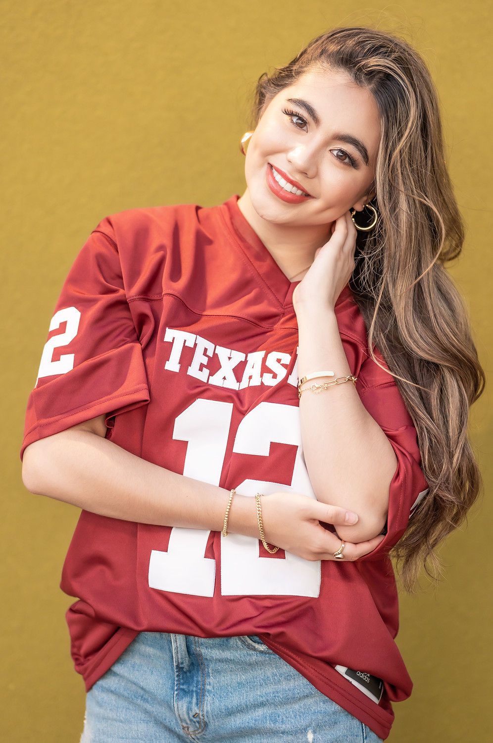 Smiling woman in Texas #12 red football jersey with gold hoop earrings and bracelets.