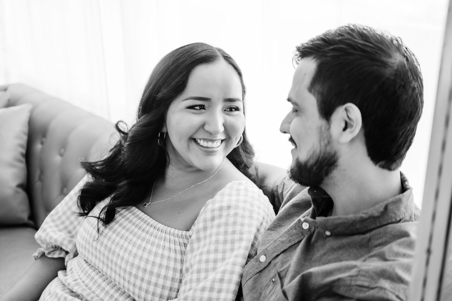 A black and white portrait of a couple sharing an intimate moment on a couch.