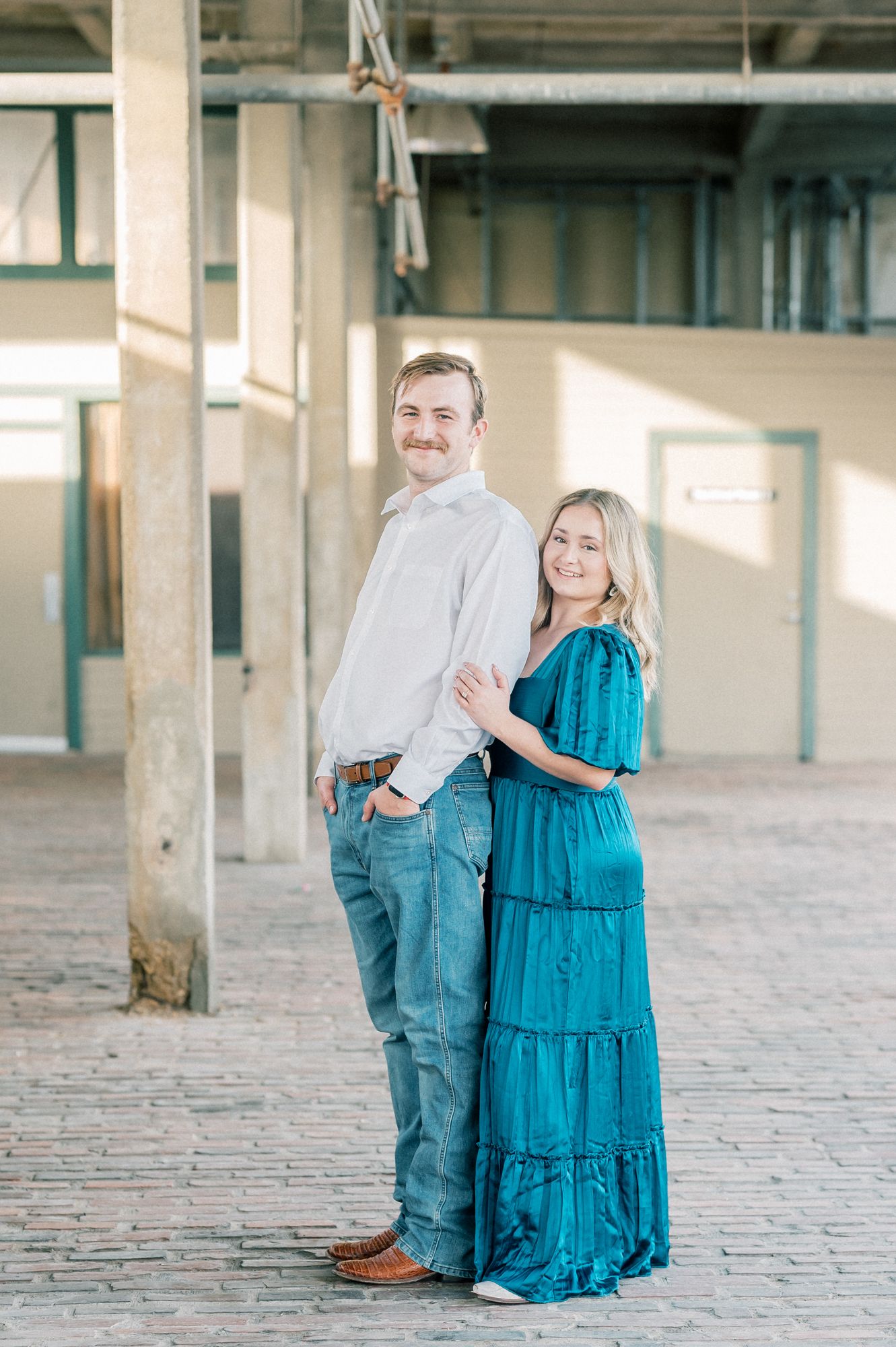A couple in coordinating blue and denim outfits poses together in a bright industrial space with concrete floors.