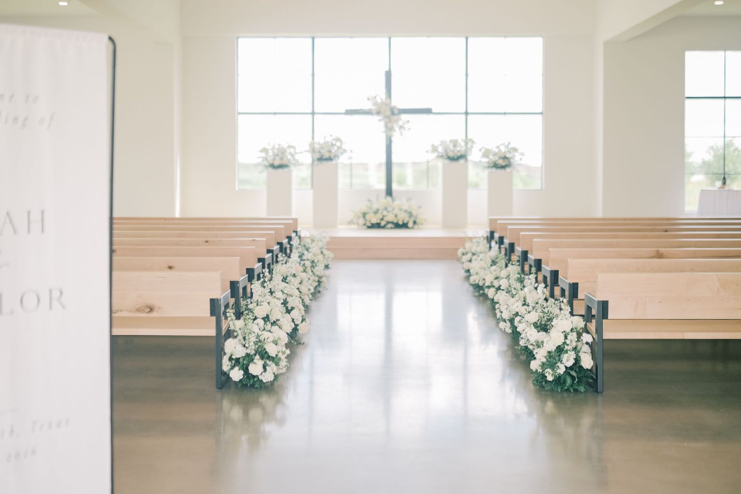 Elegant church wedding ceremony aisle decorated with white floral arrangements and candles leading to a cross altar.