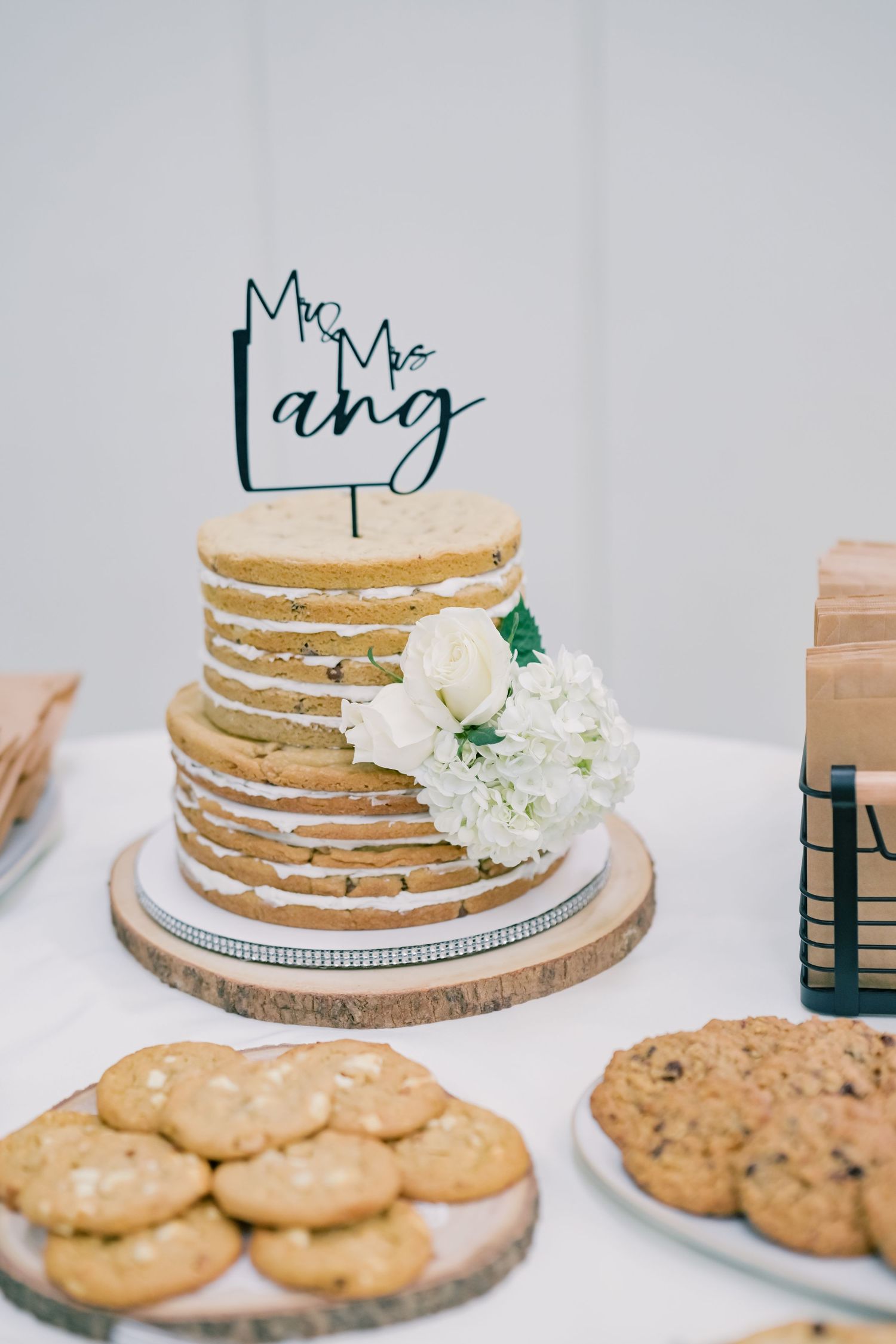 Naked cookie cake with Mr. and Mrs. Lang topper surrounded by cookies on a dessert table.
