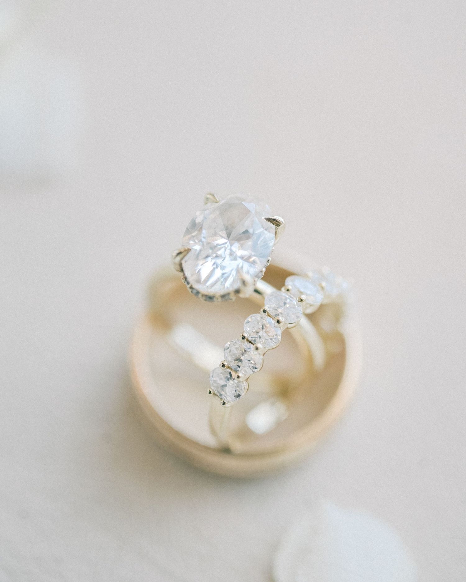 Elegant oval diamond solitaire engagement ring paired with a diamond wedding band on a gold ring holder.