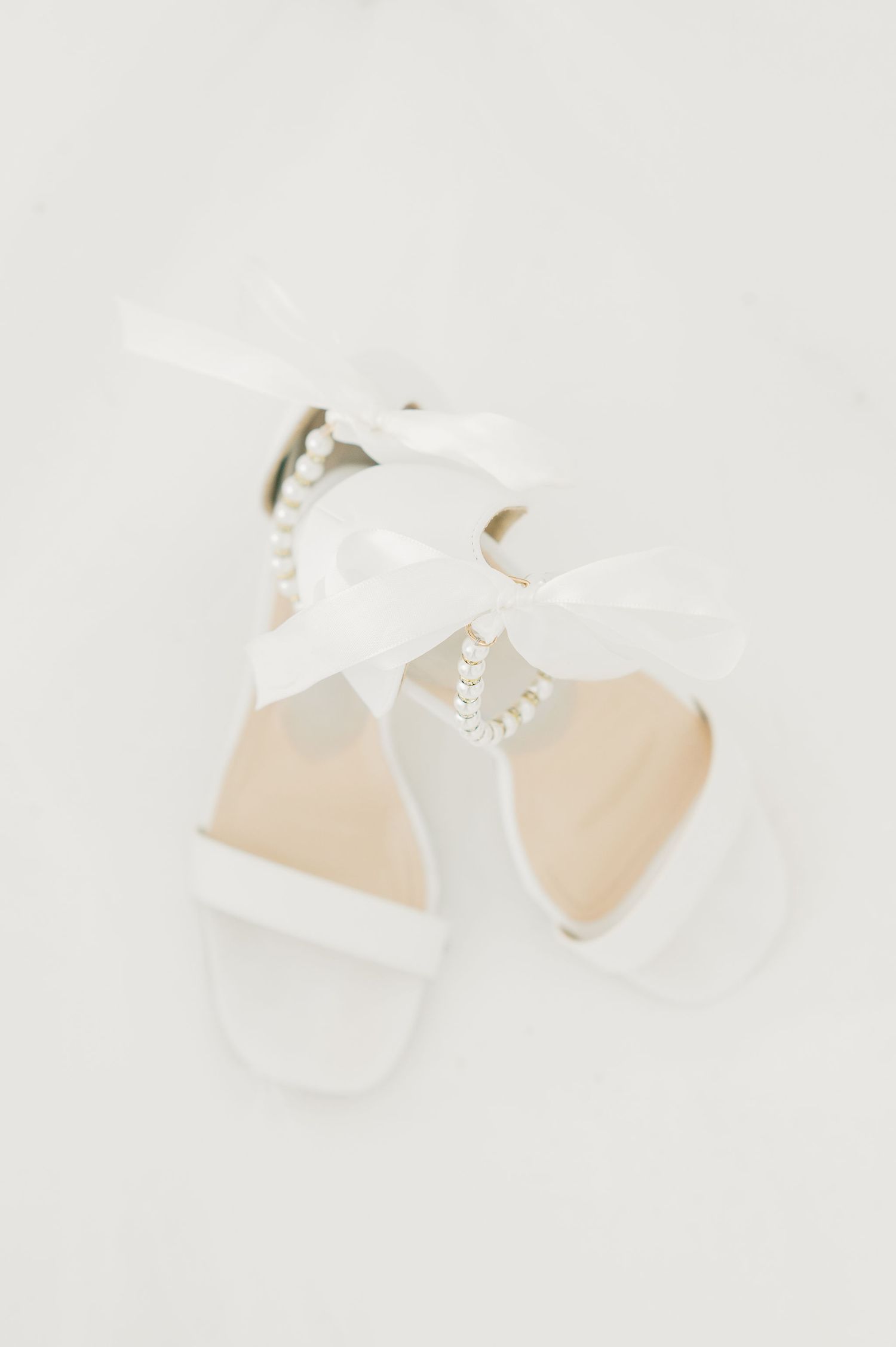White wedding shoes with delicate bows displayed on light neutral background.
