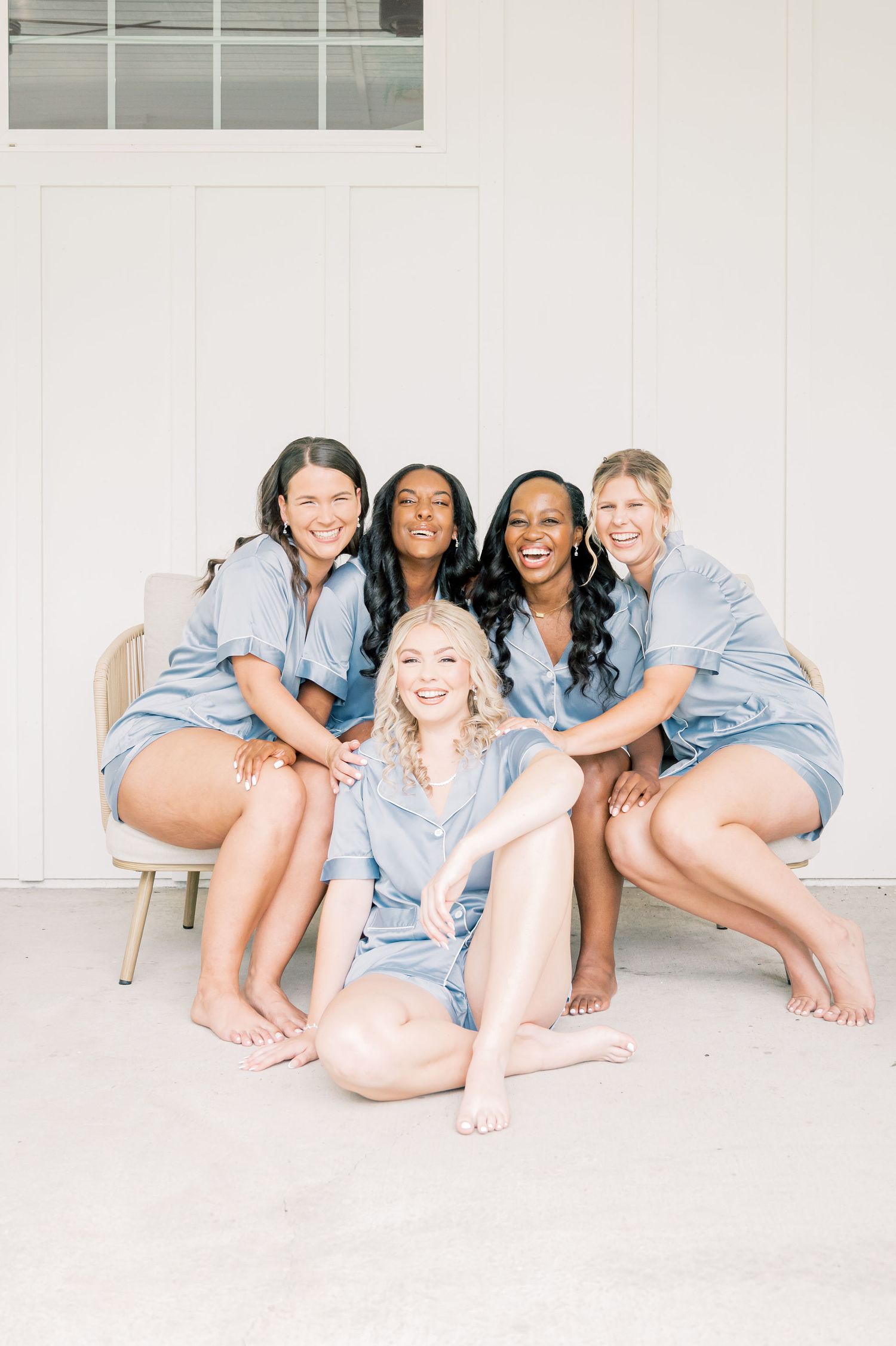 A group of bridesmaids in matching light blue robes pose playfully on the floor during wedding preparations.