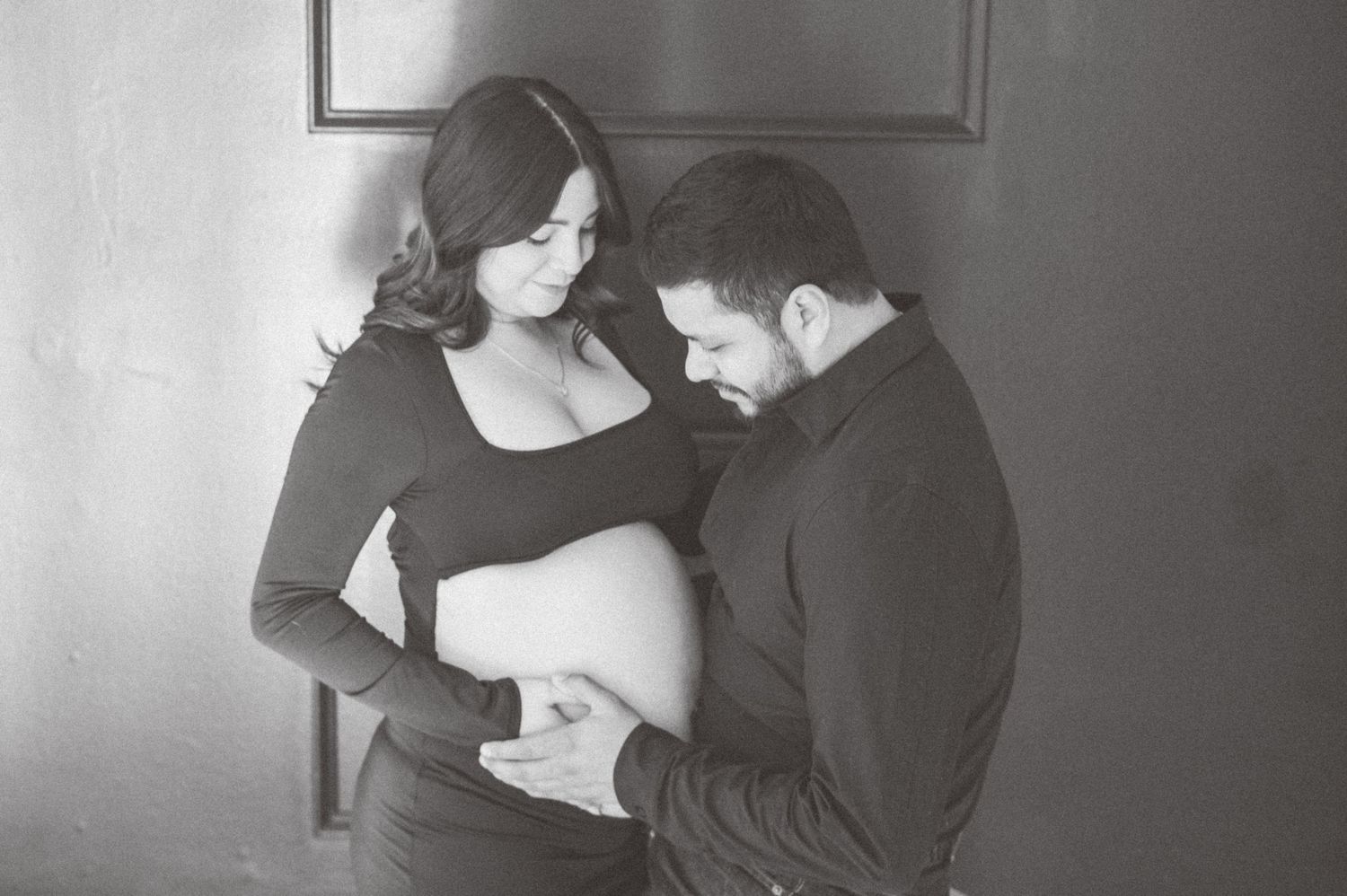 Black and white maternity photo of couple tenderly cradling pregnant belly in a studio setting.
