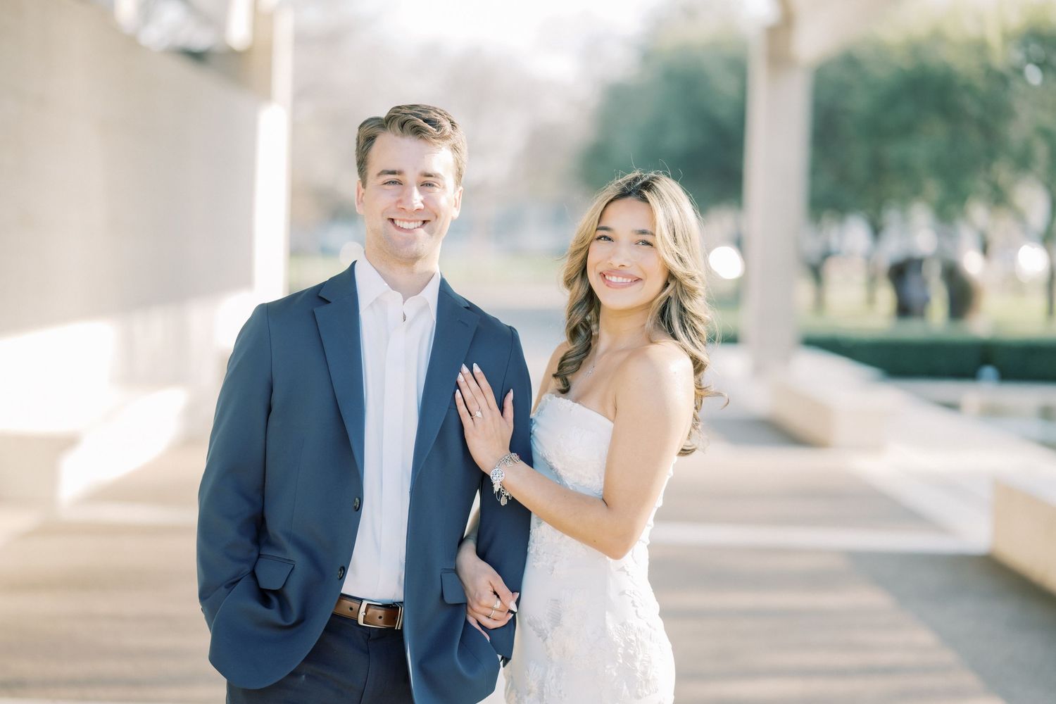 A happy couple poses together outdoors, the bride in a white dress and groom in a navy suit.