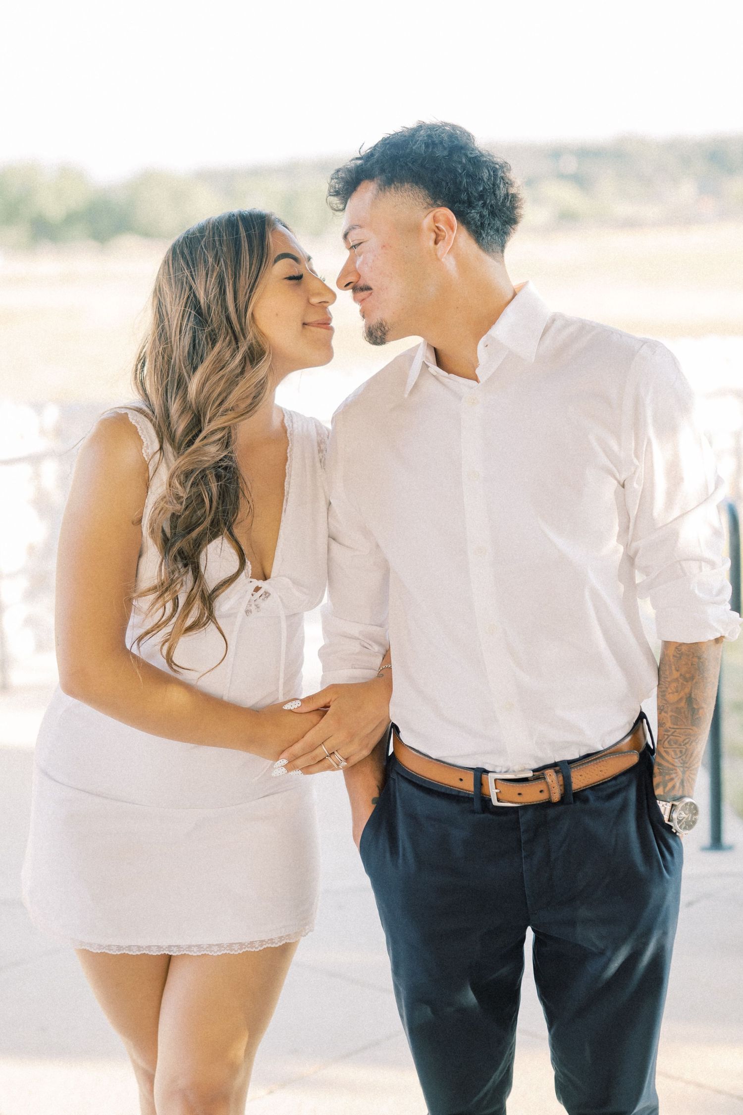 Romantic couple in coordinating white outfits sharing an intimate moment during engagement shoot.