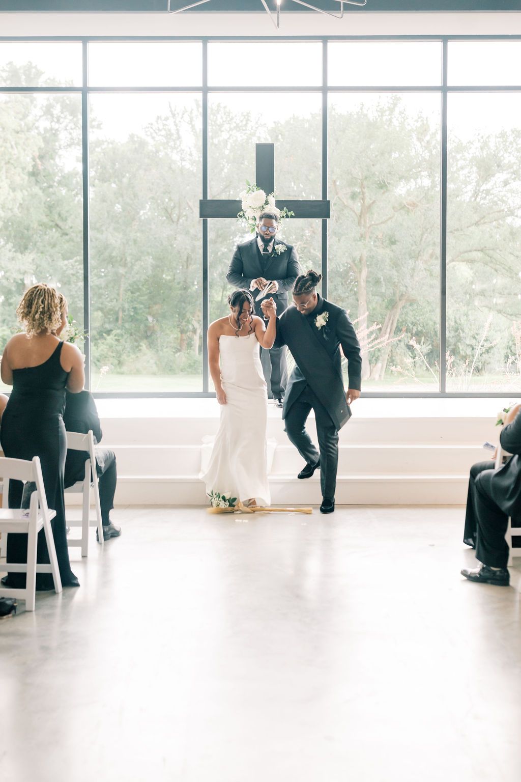 Bride and groom celebrate their recessional in a bright modern wedding venue with large windows and a floral cross.