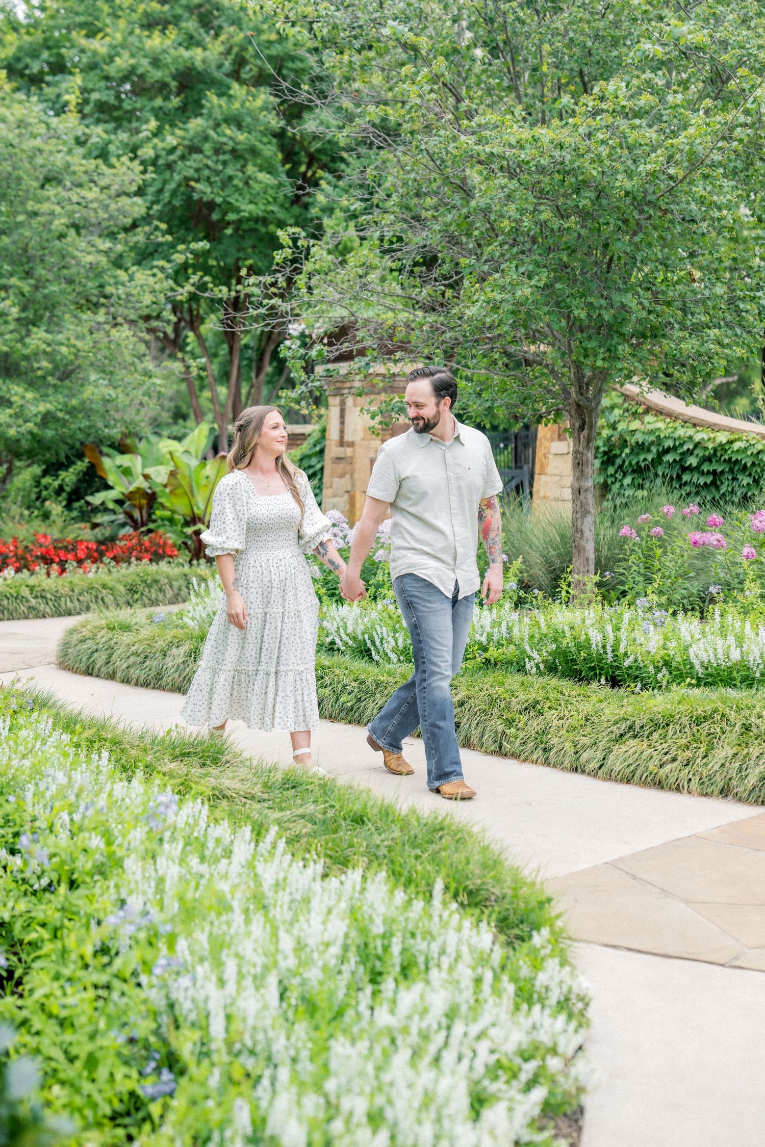 Happy couple walking hand in hand along a garden path lined with white and red flowers.
